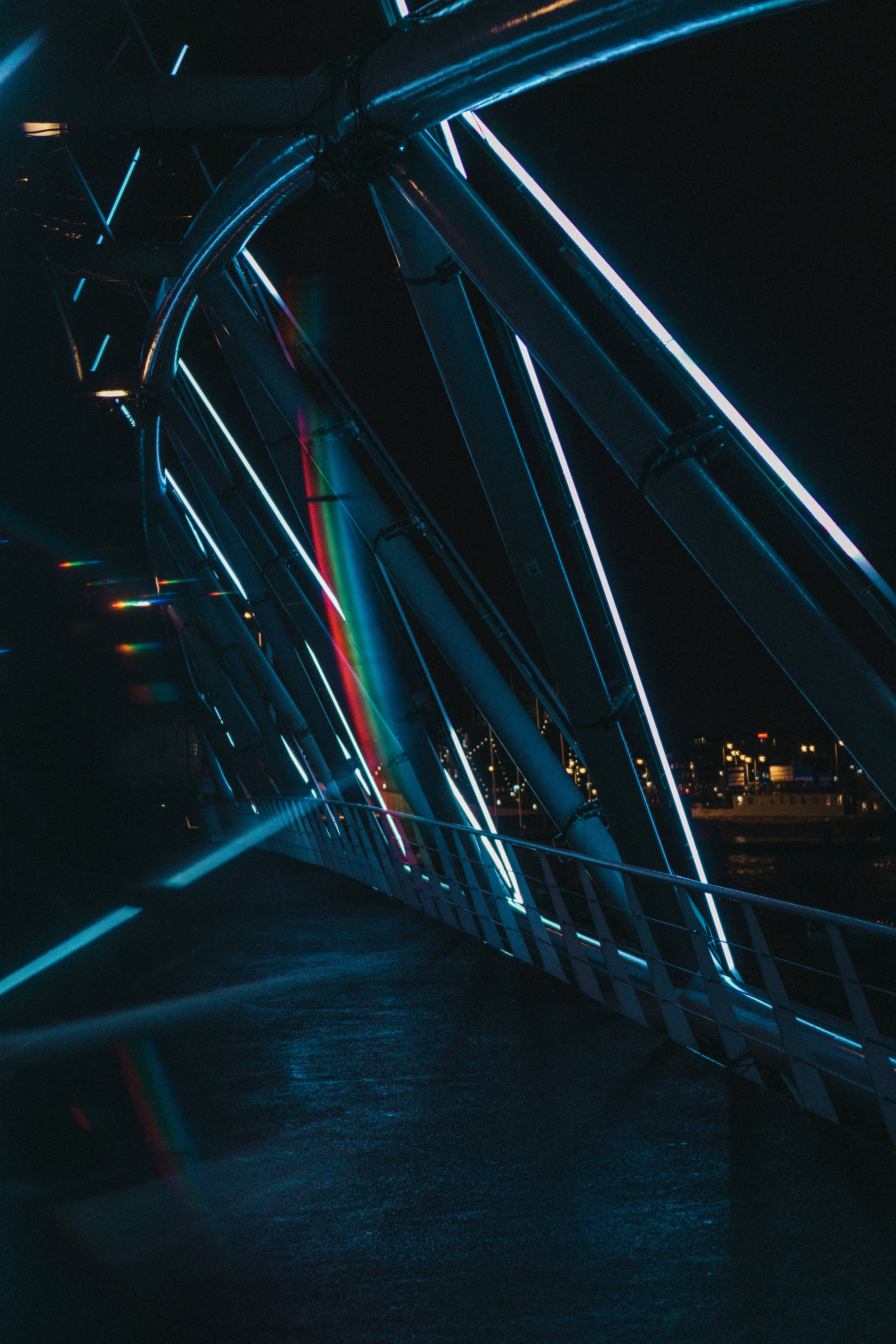dark neon iPhone 桌布 壁紙 — 一座現代橋樑的低角度夜間拍攝，帶有發光的藍色霓虹燈和彩虹鏡頭光暈。