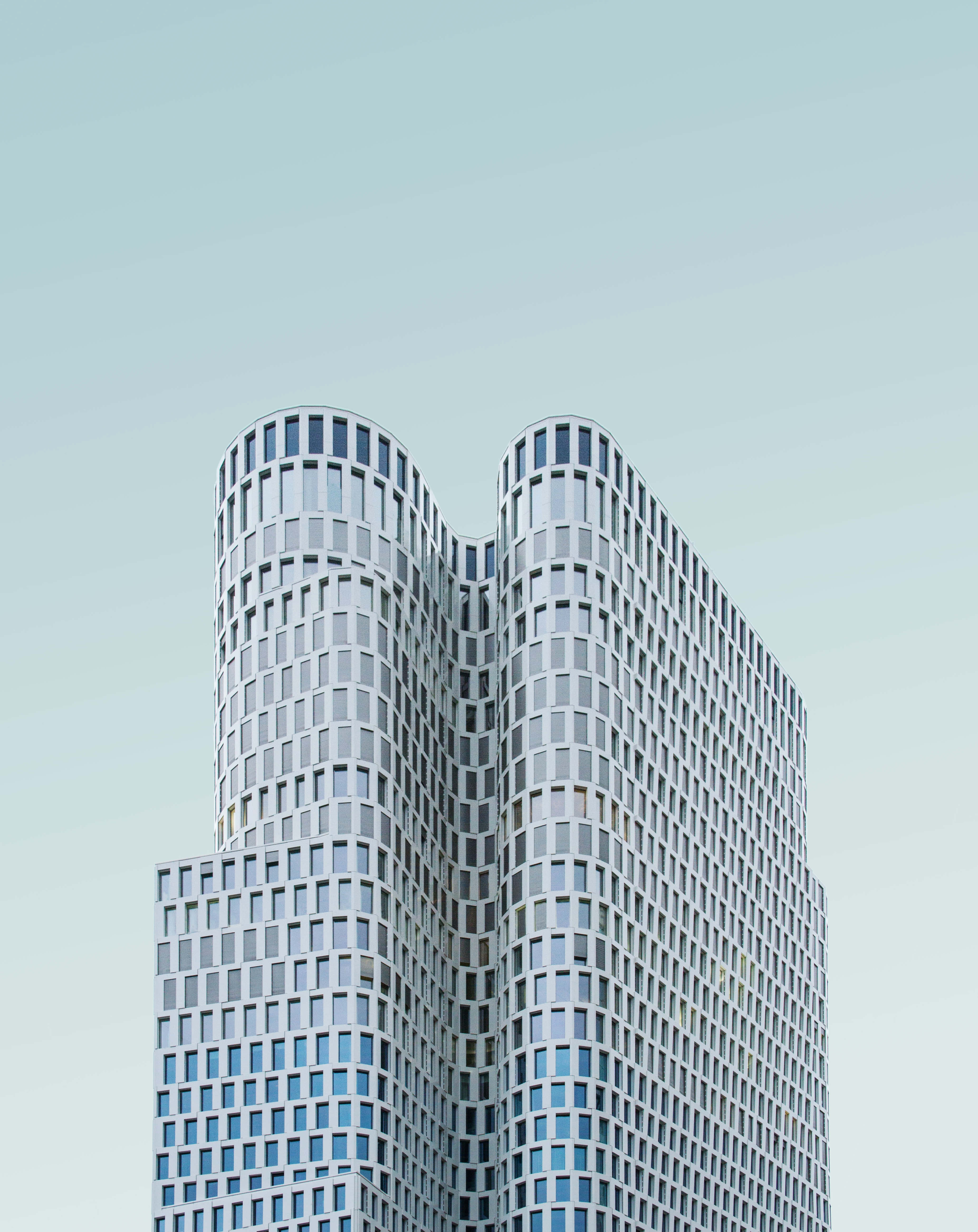 Building 桌布 壁紙 — 一座現代波浪形摩天大樓，配有玻璃窗，在極簡主義城市建築中聳立於淡藍色天空下。