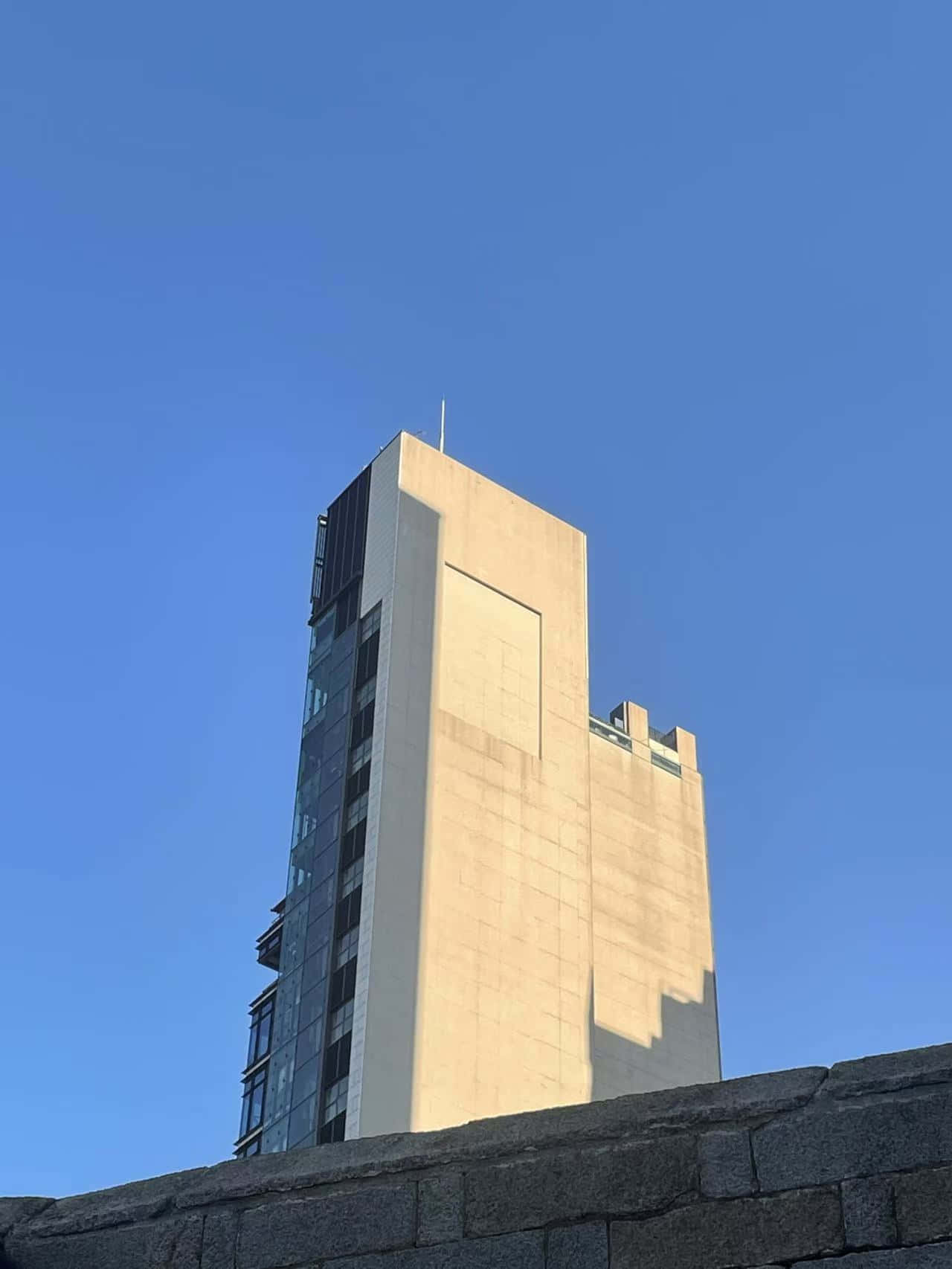 urban architecture 壁紙 — 一座現代混凝土和玻璃摩天大樓在晴朗的藍天下聳立，陽光投射出強烈的陰影。