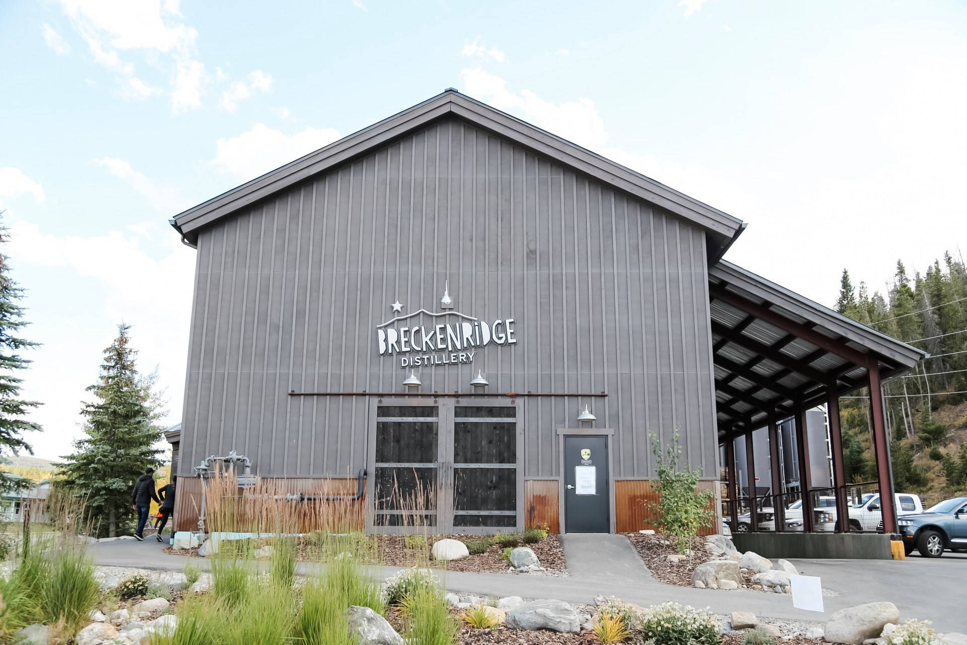Colorado 桌布 壁紙 — 一座現代灰色穀倉風格的釀酒廠建築，帶有 'Breckenridge Distillery' 標誌，矗立在綠化和松樹之中，天空部分多雲。