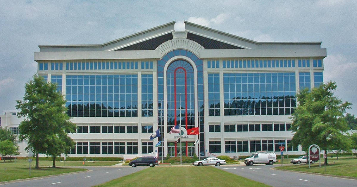 Building 桌布 壁紙 — 一座現代玻璃和白色辦公樓，帶有拱形窗戶和旗幟，矗立在多雲的天空下，附近停有汽車。