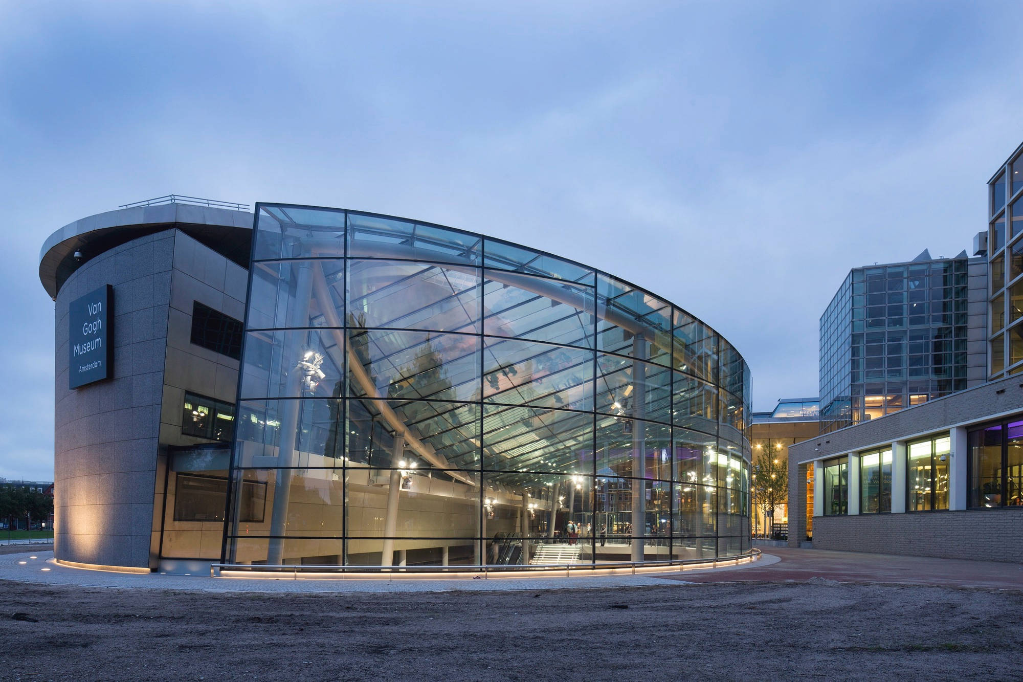 Netherlands 桌布 壁紙 — 一座現代玻璃和鋼結構的博物館建築在黃昏時溫暖地發光，映照著天空和室內燈光。
