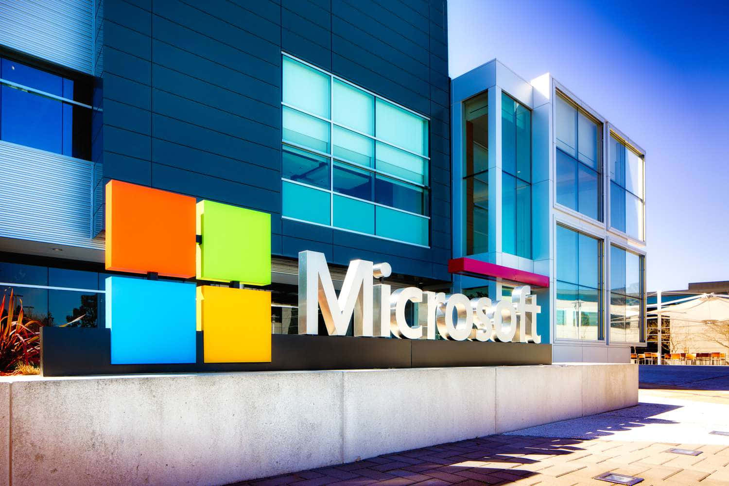 陽光明媚的日子裡，Microsoft企業建築帶有彩色標誌和玻璃外牆。 — Microsoft 壁紙