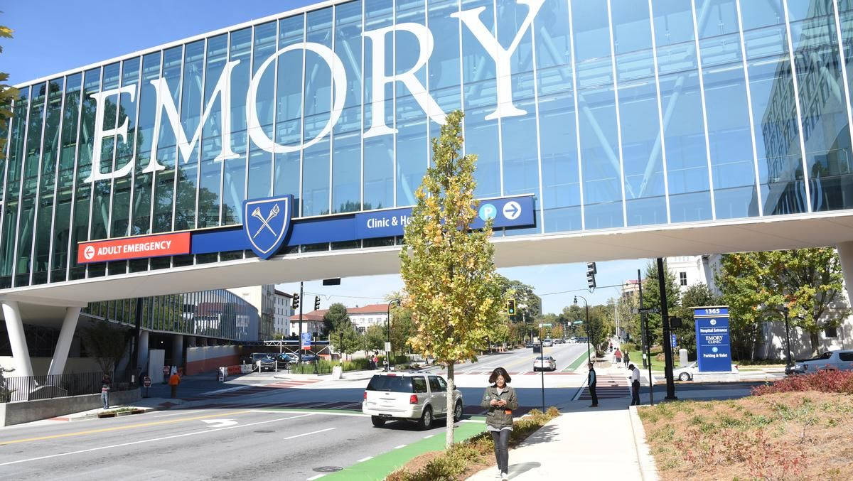 Buildings 桌布 壁紙 — 一座現代玻璃建築，帶有「EMORY」標誌，聳立在陽光明媚、有行人和汽車的街道上。