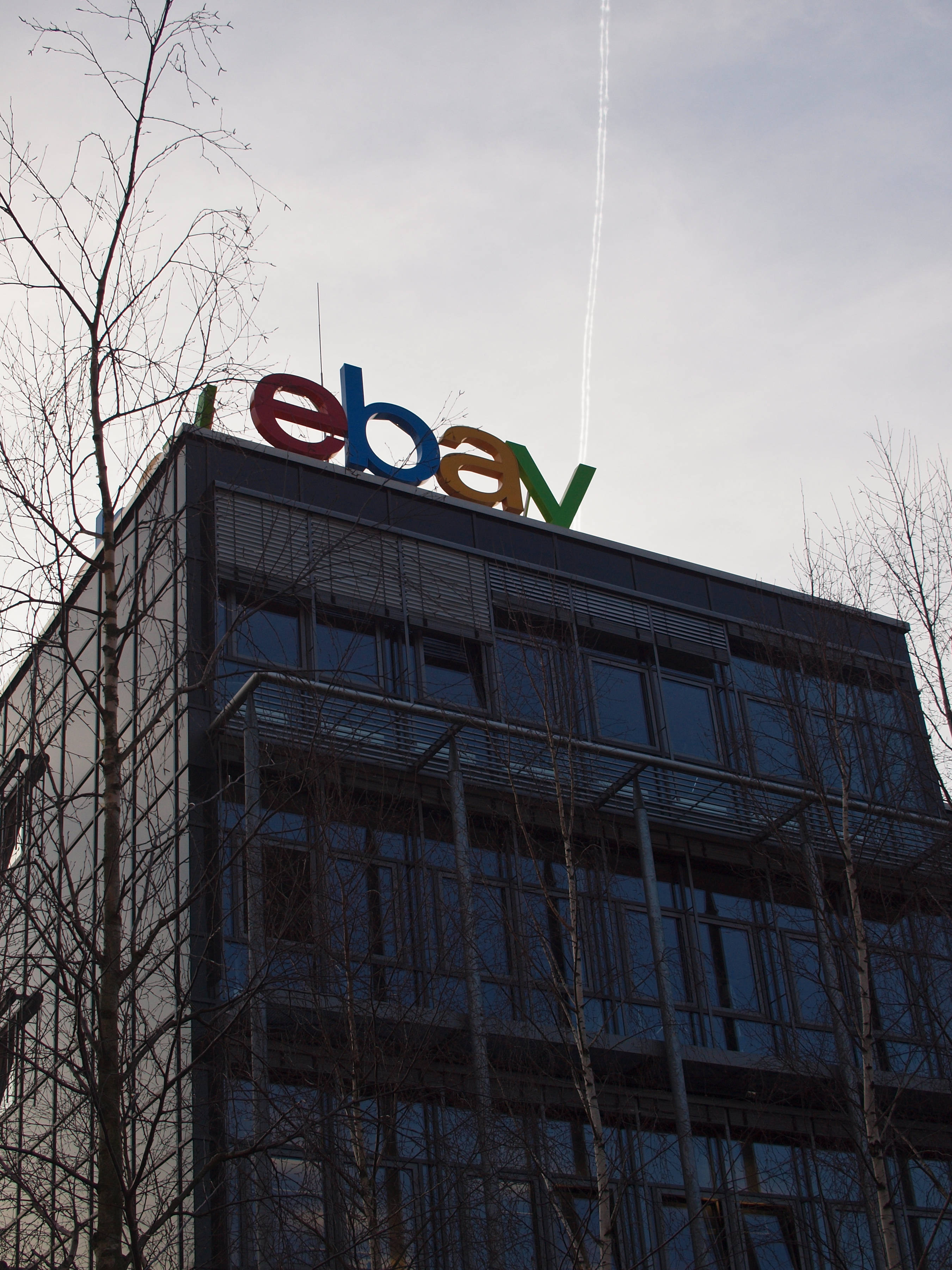 eBay 桌布 壁紙 — 一座現代玻璃建築，頂部有色彩繽紛的eBay標誌，襯著蒼白的天空，光禿禿的樹木框住畫面。