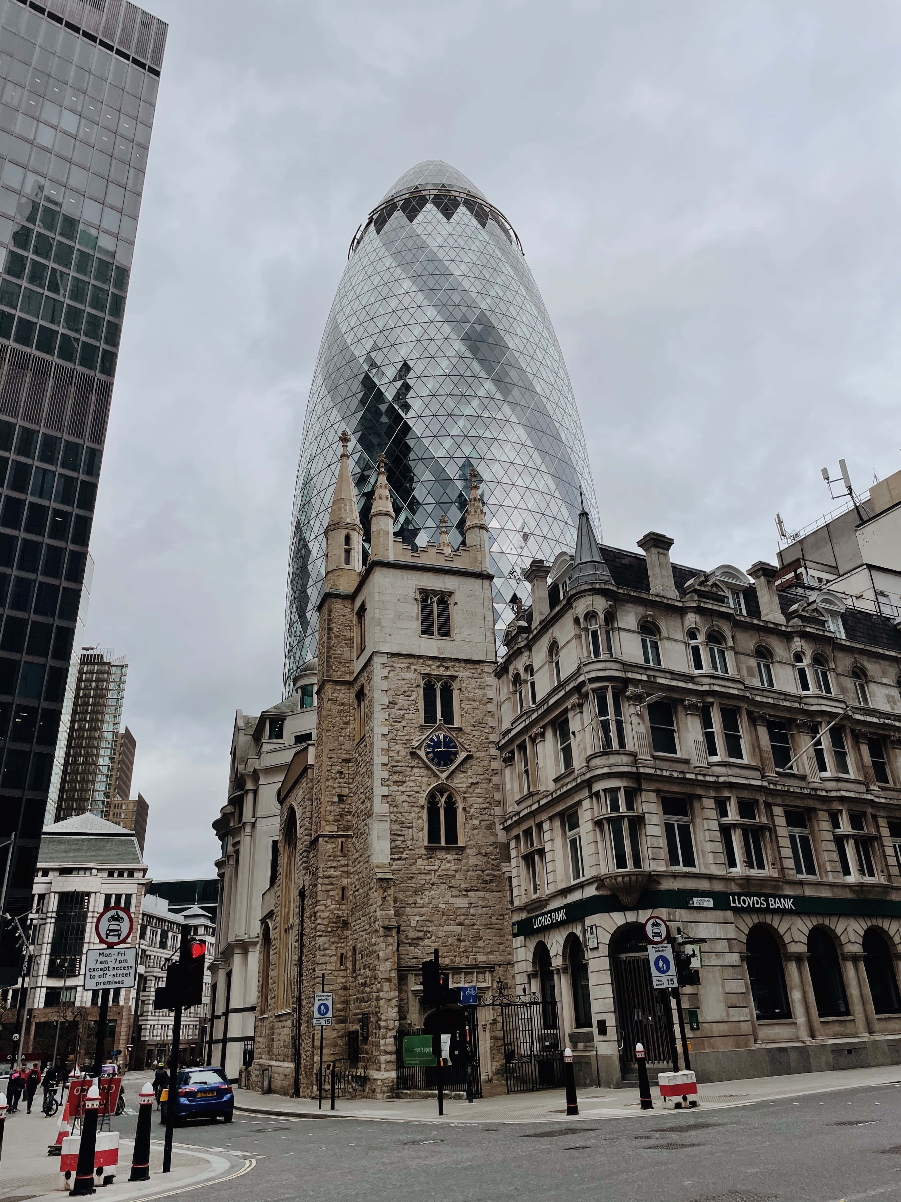 Skyscraper 桌布 壁紙 — 一座現代玻璃摩天大樓，具有獨特的圓形形狀，在陰天籠罩下聳立於歷史石砌建築之上。