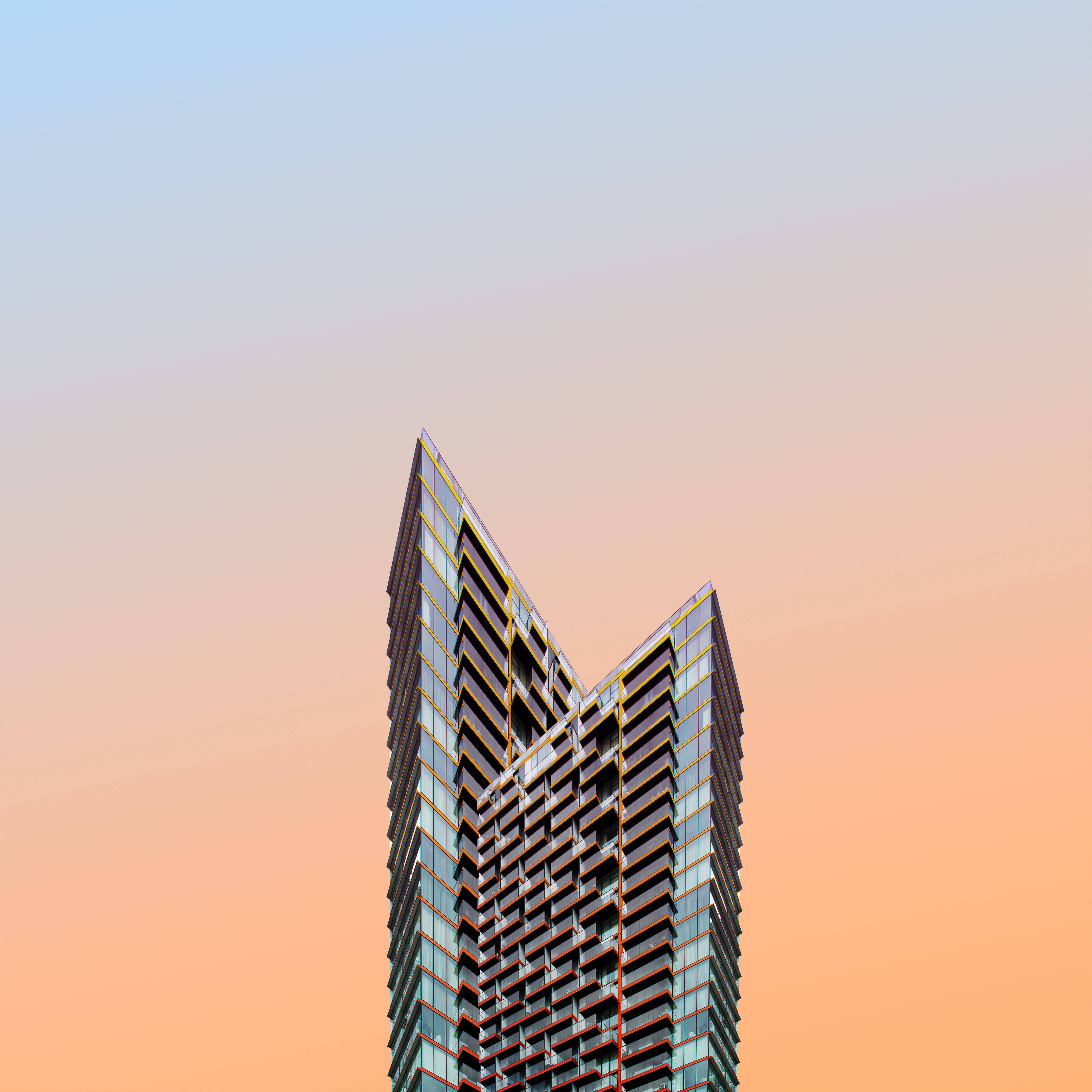 Architecture 桌布 壁紙 — 一座現代玻璃摩天大樓，帶有幾何陽台，刺穿從柔和藍色過渡到溫暖桃色的漸變天空。