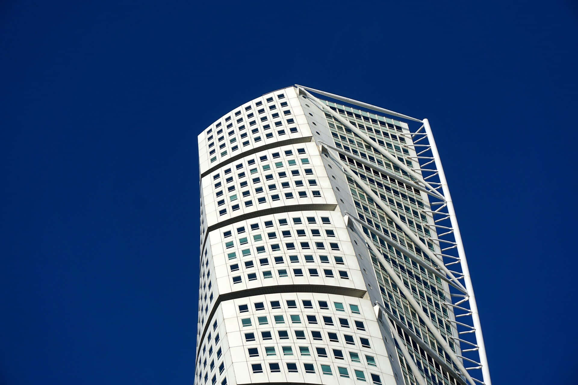 Blue Sky 桌布 壁紙 — 一座現代白色摩天大樓，擁有弧形外牆和玻璃窗，在深藍色的天空下巍然聳立。