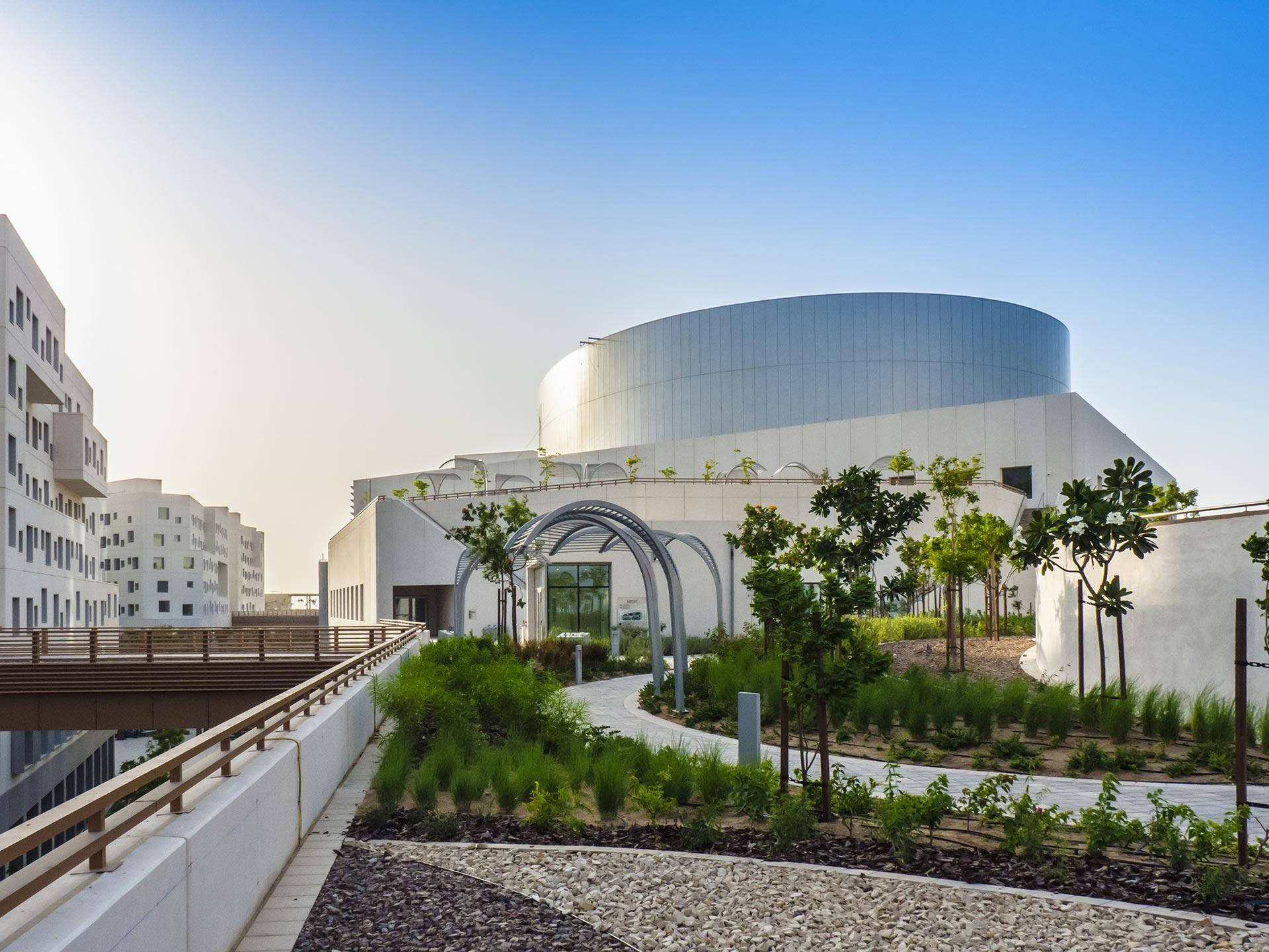 建築 桌布 壁紙 — 一座現代白色曲線建築，設有綠色屋頂花園和蜿蜒小徑，在晴朗的藍天下。