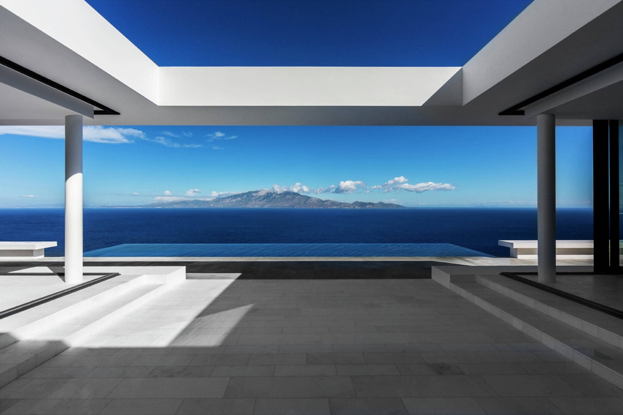 Luxury House 桌布 壁紙 — 一座現代白色涼亭俯瞰著廣闊的藍色海洋，遠處有山脈，天空晴朗。