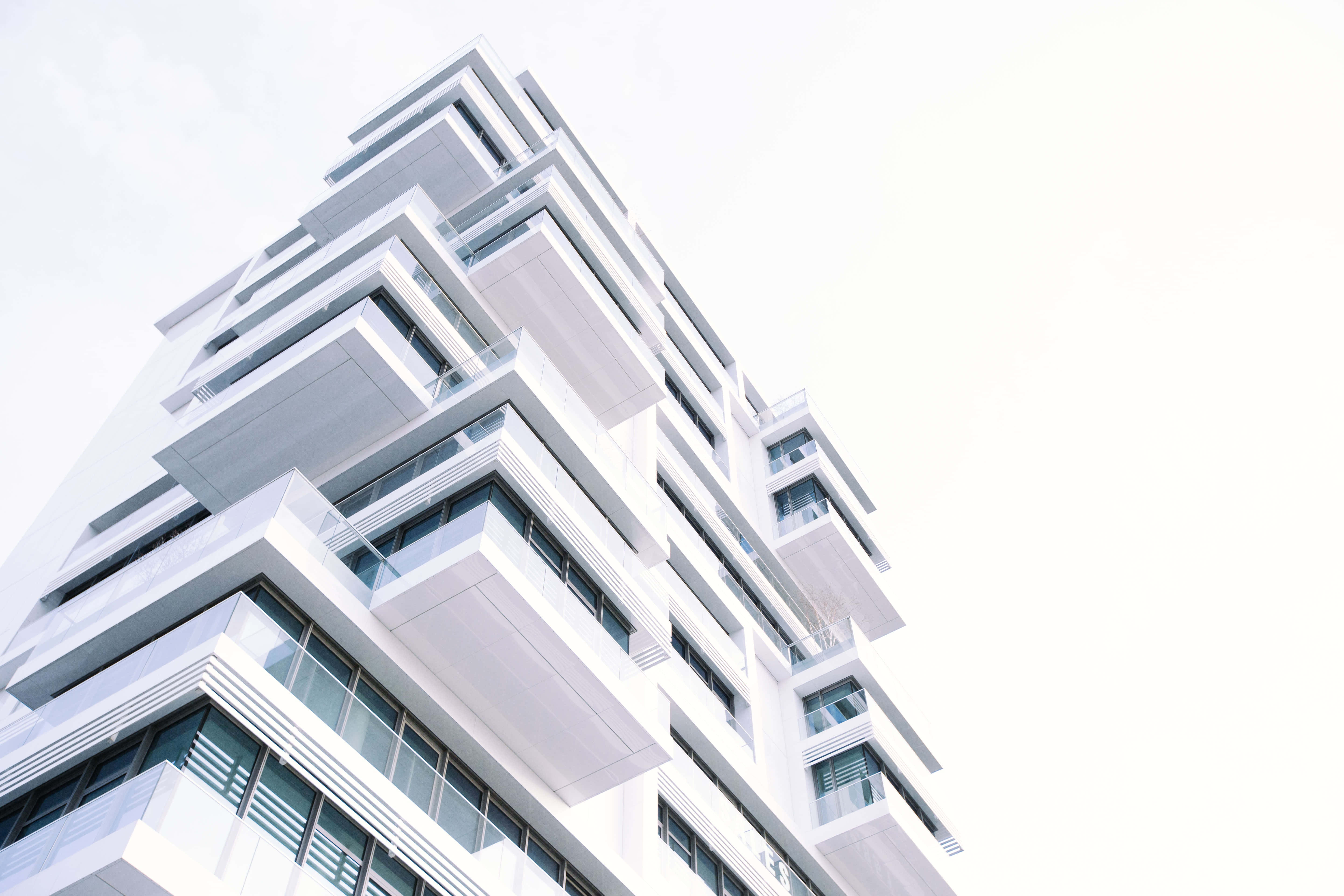 Building 桌布 壁紙 — 一座現代白色高層建築，帶有玻璃陽台，在明亮的天空下向上傾斜。