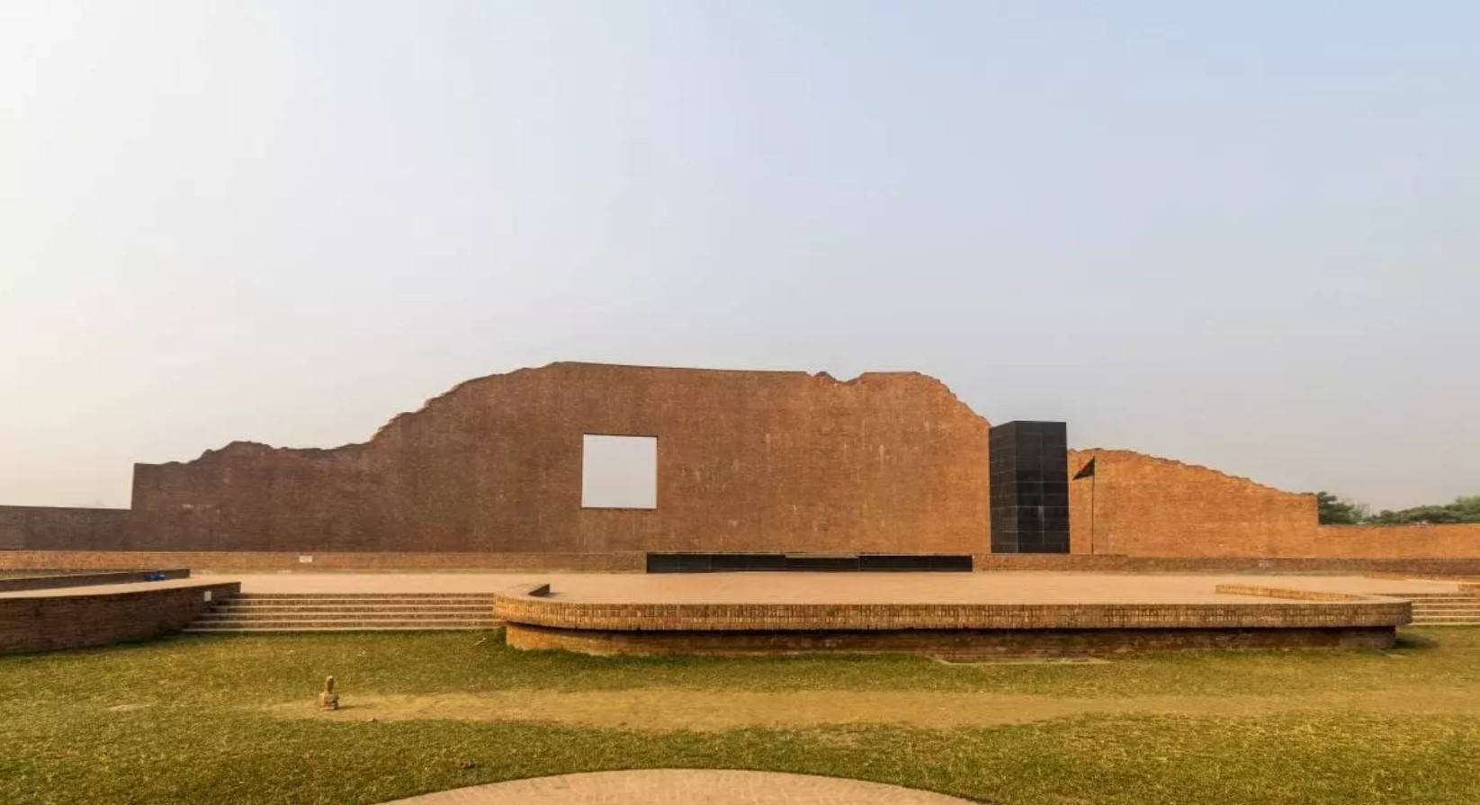 Dhaka 桌布 壁紙 — 一座現代磚砌博物館，帶有一個大方形窗戶，矗立在朦朧天空下的古代遺跡旁。