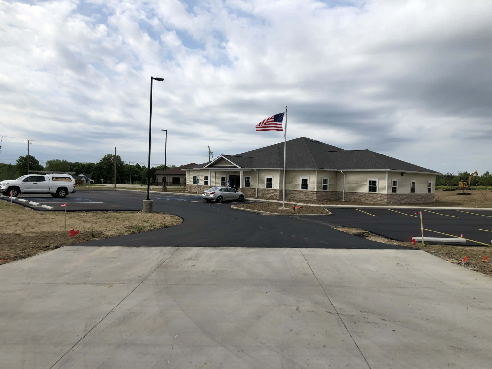 Ashland County 桌布 壁紙 — 一座現代米色建築，深色屋頂，美國國旗在陰天飄揚，汽車停在新鋪設的停車場。