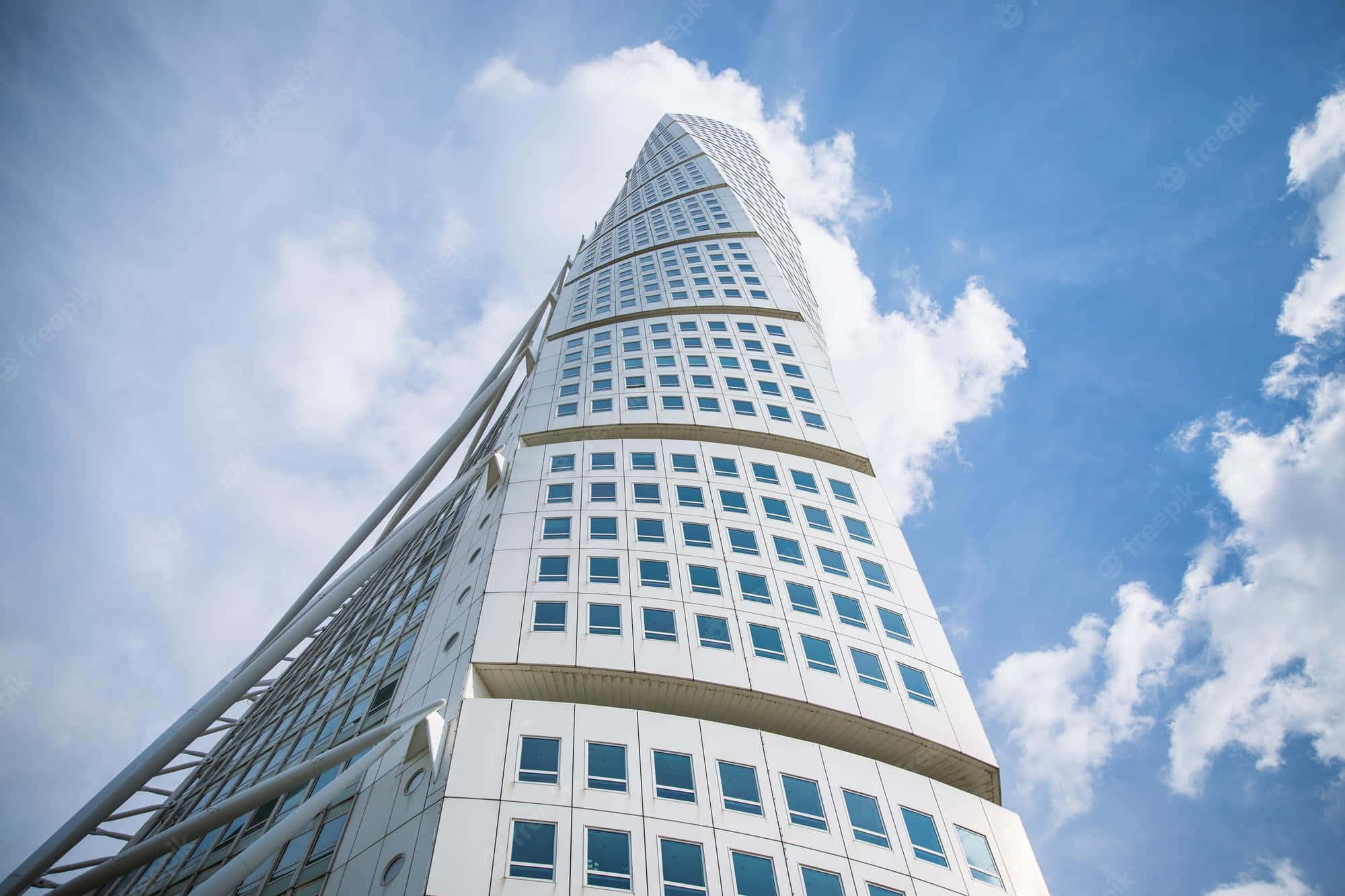 Skyscraper 桌布 壁紙 — 一座現代螺旋形玻璃窗摩天大樓在明亮的藍天和 fluffy 白雲襯托下聳立。