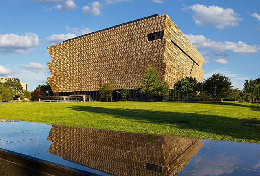 Smithsonian 桌布 壁紙 — 一座現代金色格柵建築在藍天白雲下倒映在深色水池中。