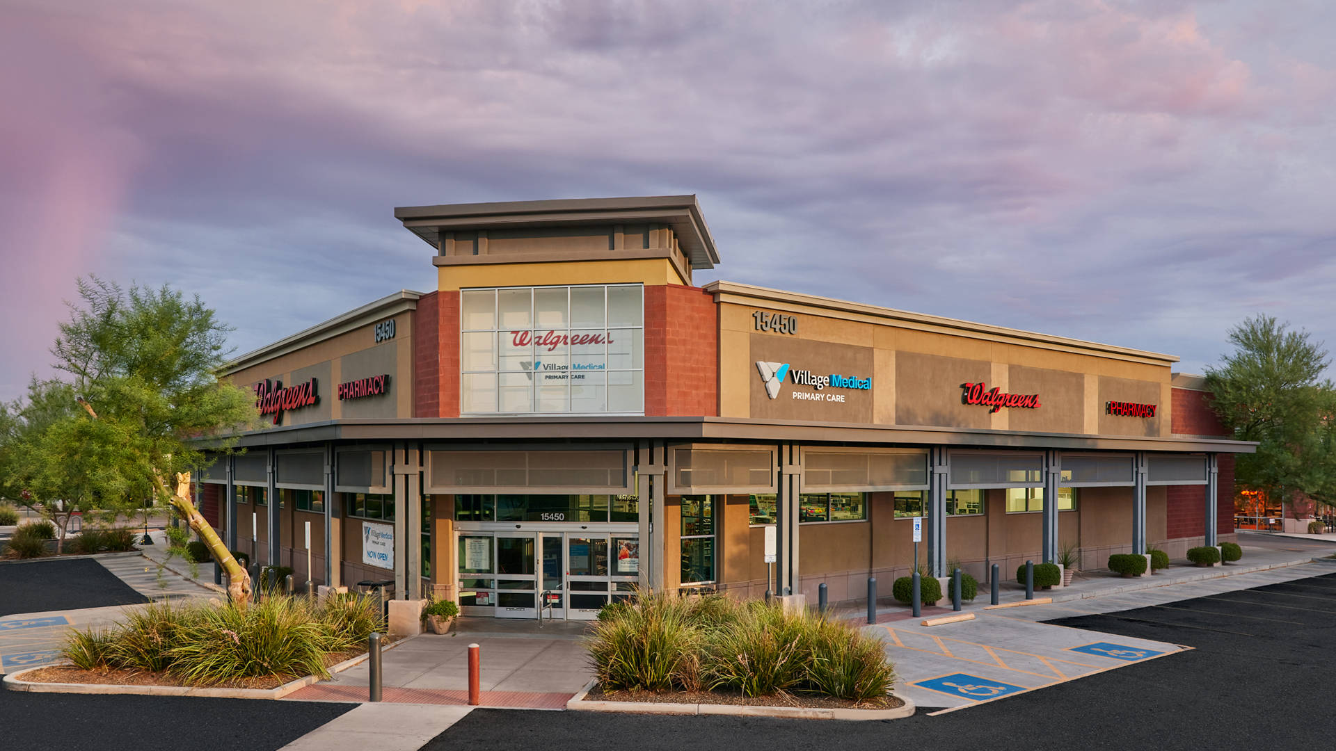 Business 桌布 壁紙 — 一座現代零售建築，帶有Walgreens和Village Medical標誌，背景是戲劇性的粉紅和紫色日落天空。