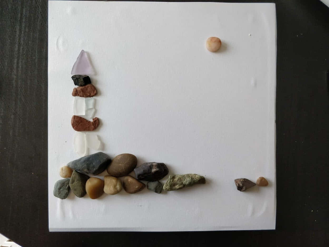 Sea Glass 桌布 壁紙 — 一座由各種光滑石頭和玻璃片製成的燈塔，矗立在白色泡沫底座上，背景為深色。