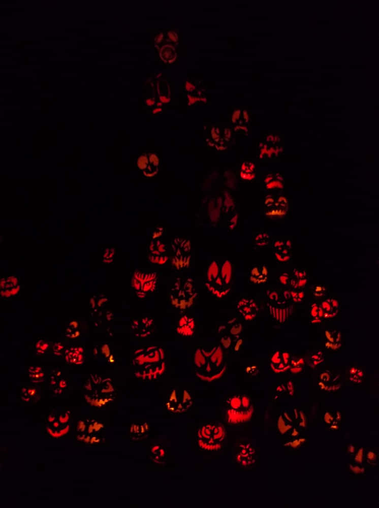 Jack O Lantern 桌布 壁紙 — 一座由發光的傑克南瓜燈堆疊而成的高聳金字塔，帶有各種恐怖面孔，照亮了黑暗。