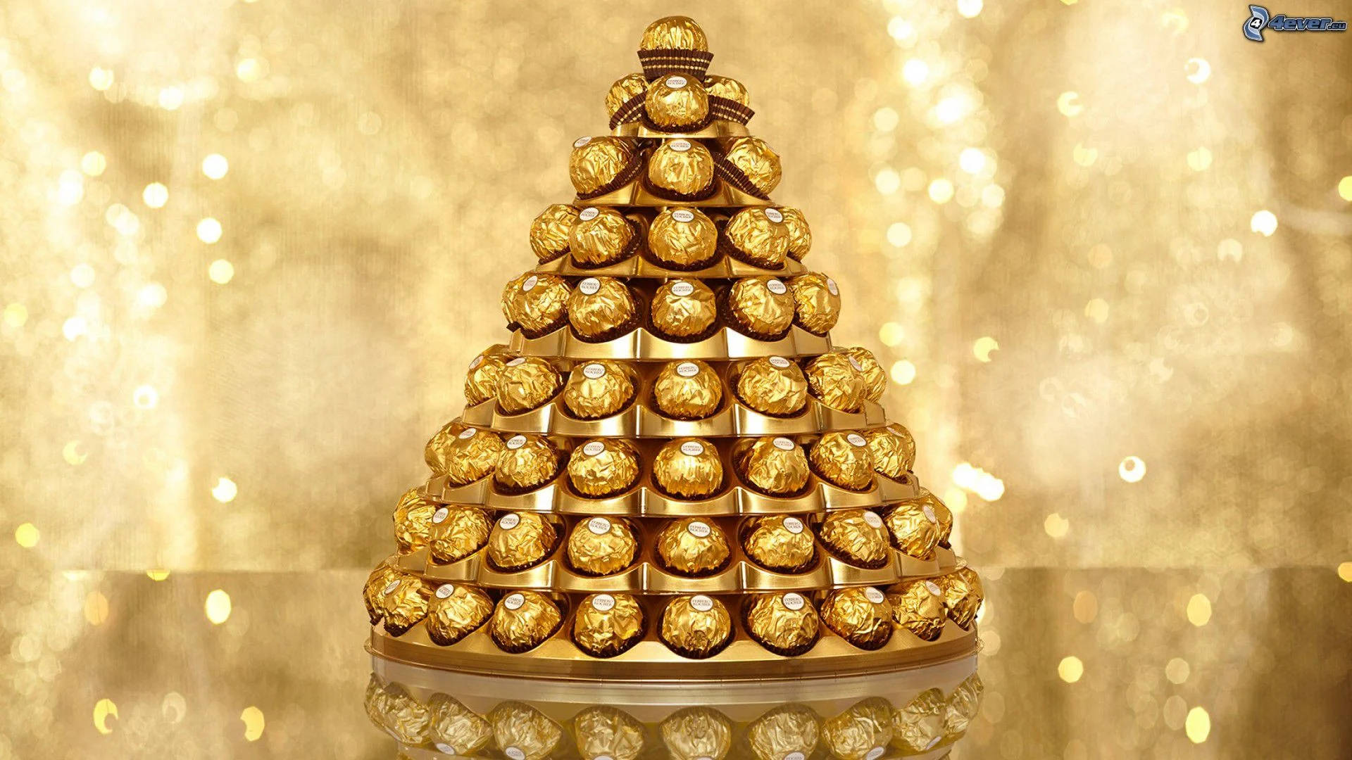 Foil 桌布 壁紙 — 一座由金色包裝的費列羅 Rocher 巧克力堆成的金字塔，在閃爍的金色散景背景下閃耀。