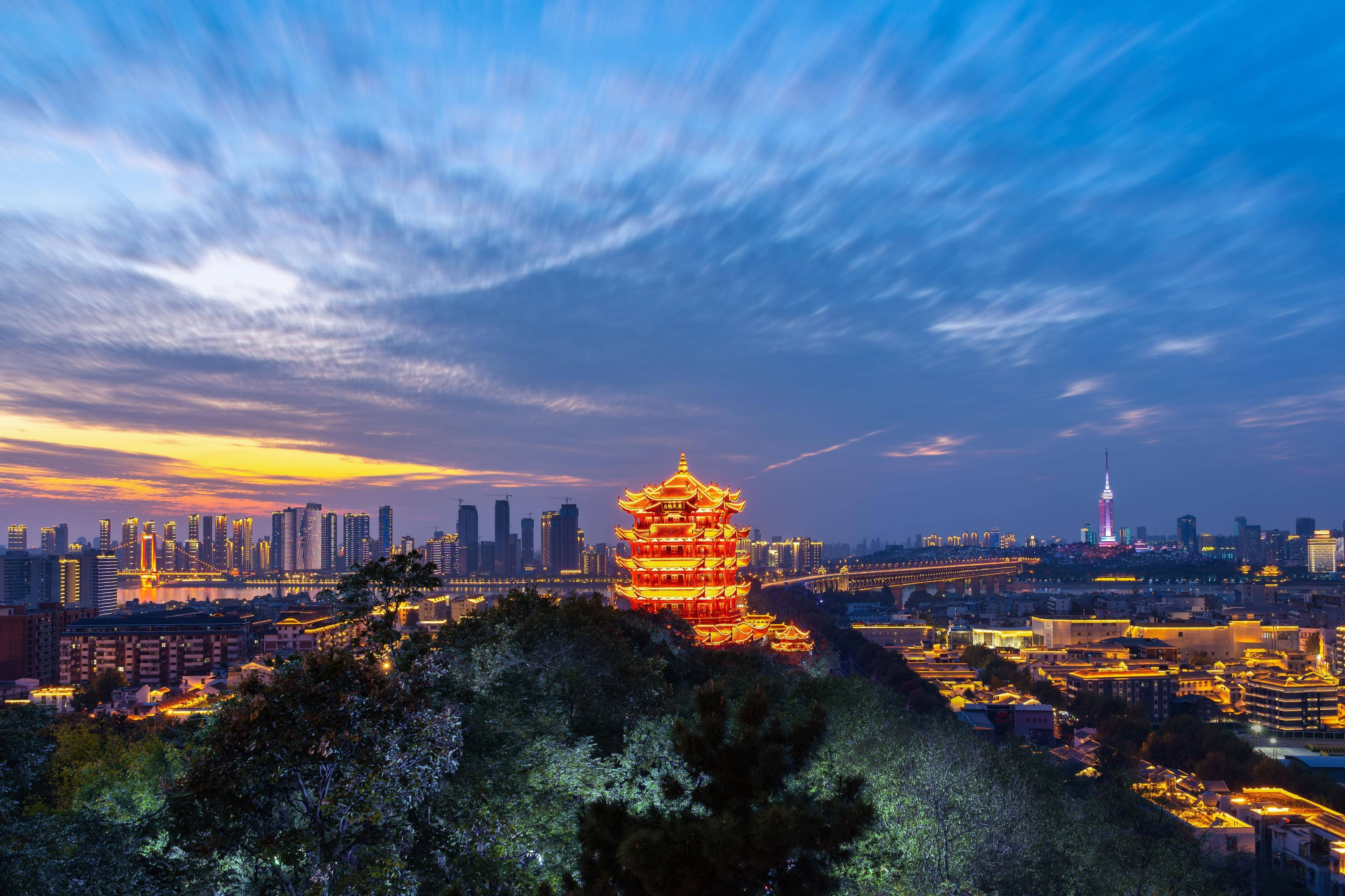 Wuhan 桌布 壁紙 — 一座發光的傳統寶塔在山頂上俯瞰著暮色中廣闊的城市景觀，帶有條紋雲和溫暖的燈光。