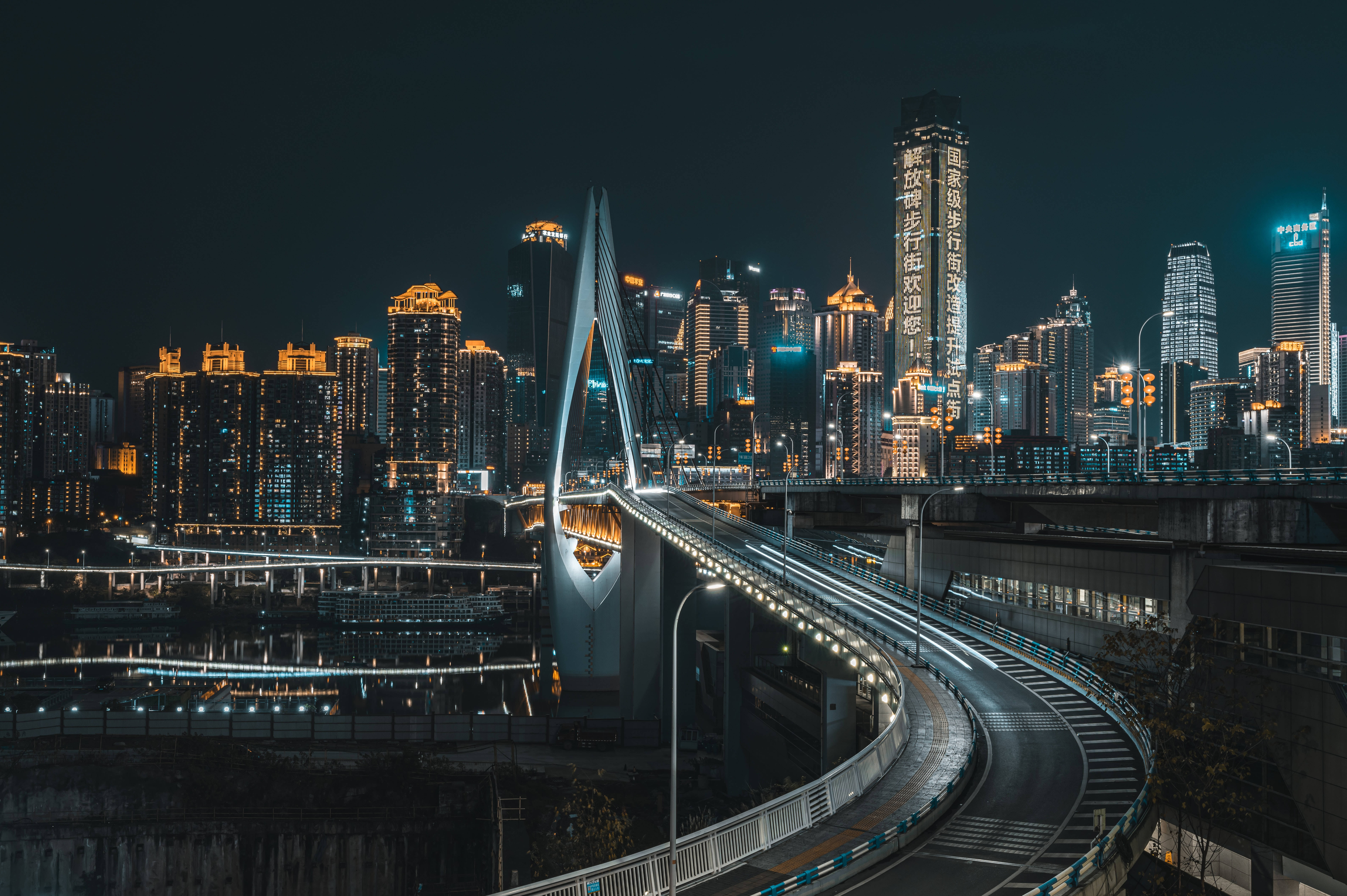 Full 4K 桌面 桌布 壁紙 — 一座發光的現代橋樑在密集的城市夜景中蜿蜒，伴隨著燈火通明的摩天大樓和交通的光跡。
