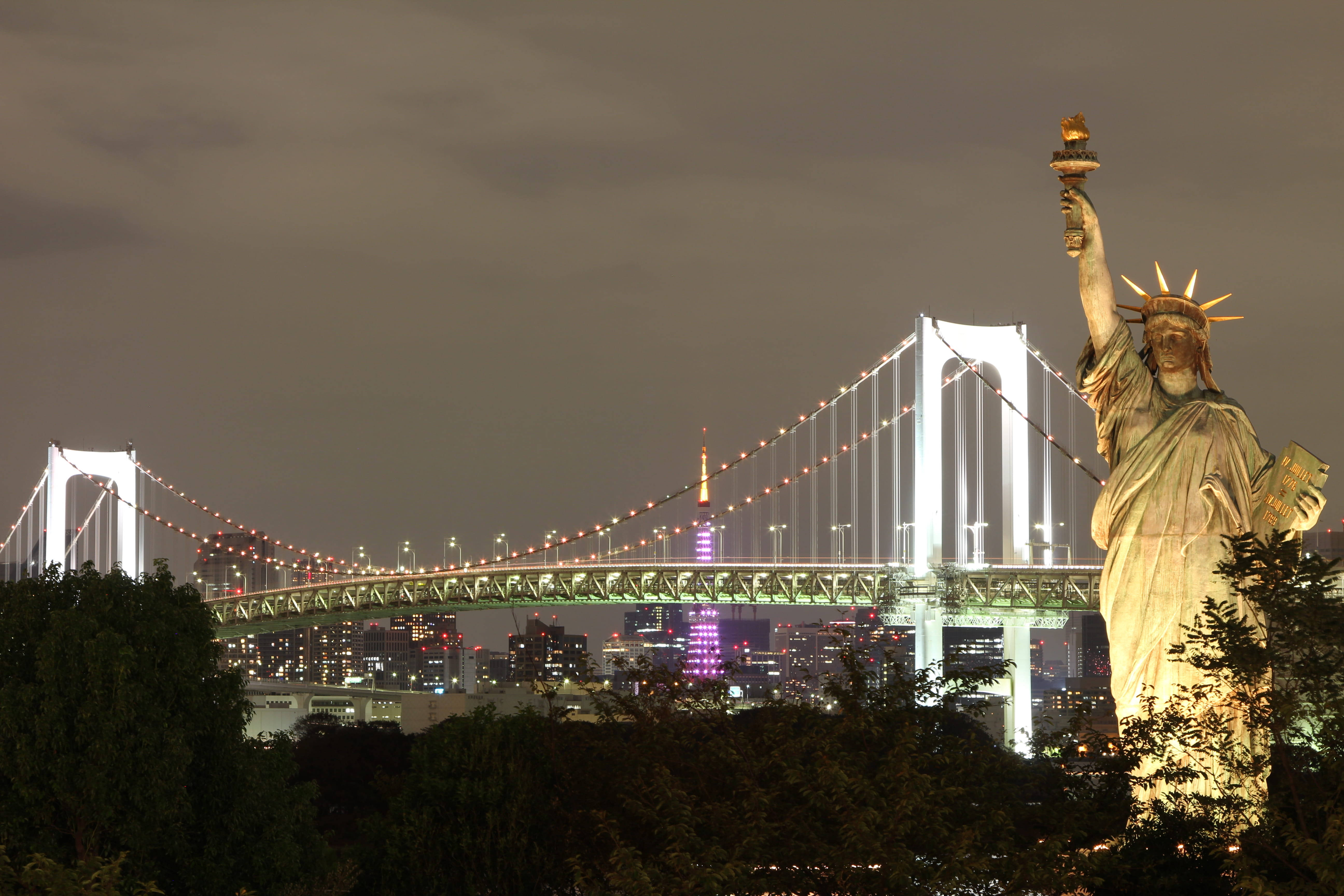new york 4K 桌布 壁紙 — 一座發光的自由女神像複製品在夜晚矗立於東京亮燈的彩虹橋前。