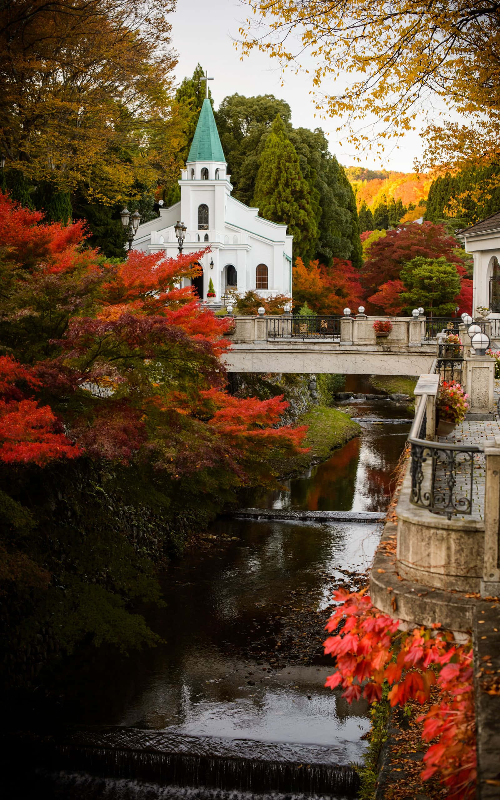 Beautiful Autumn 桌布 壁紙 — 一座白色教堂，帶有綠色尖頂，靜靜地矗立在石橋旁，橋下溪水潺潺，周圍是火紅和金黃的秋葉，色彩斑斕。