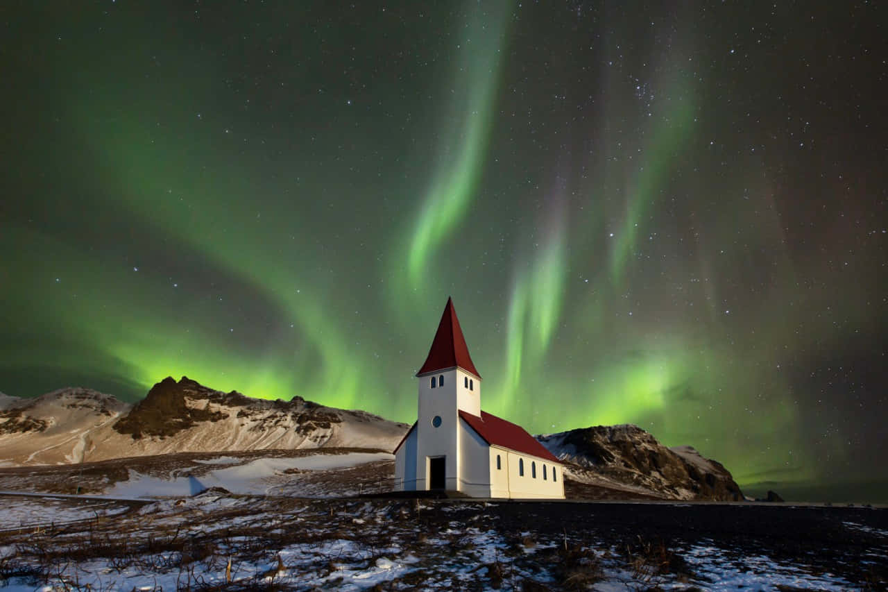 aurora borealis 桌布 壁紙 — 一座白色教堂配紅色屋頂，獨自矗立在充滿活力的綠色北極光下，北極光在繁星點點的冬日天空中舞動。