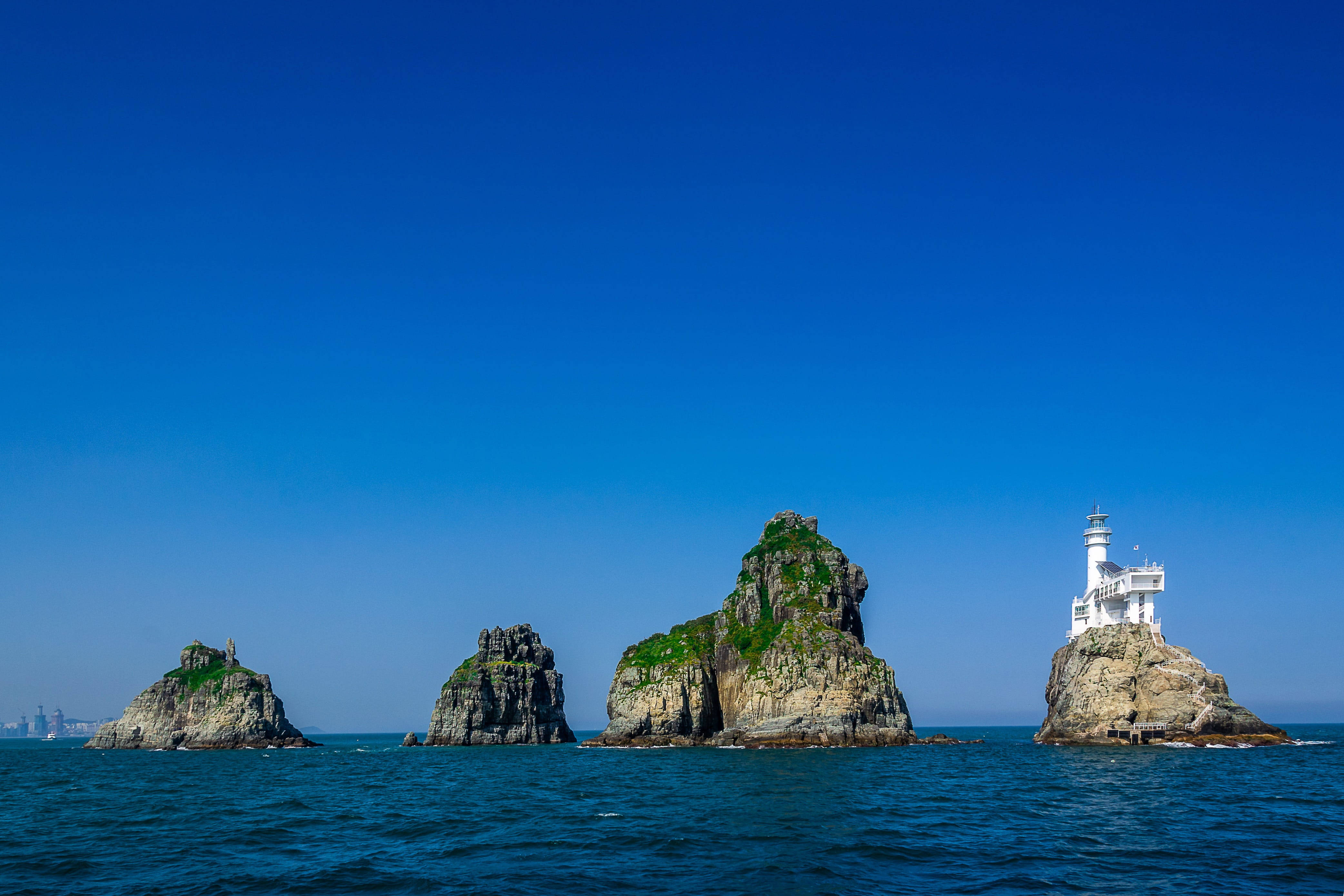 Busan 桌布 壁紙 — 一座白色燈塔棲息在岩石島上，下方是廣闊清澈的藍天和寧靜的海水。