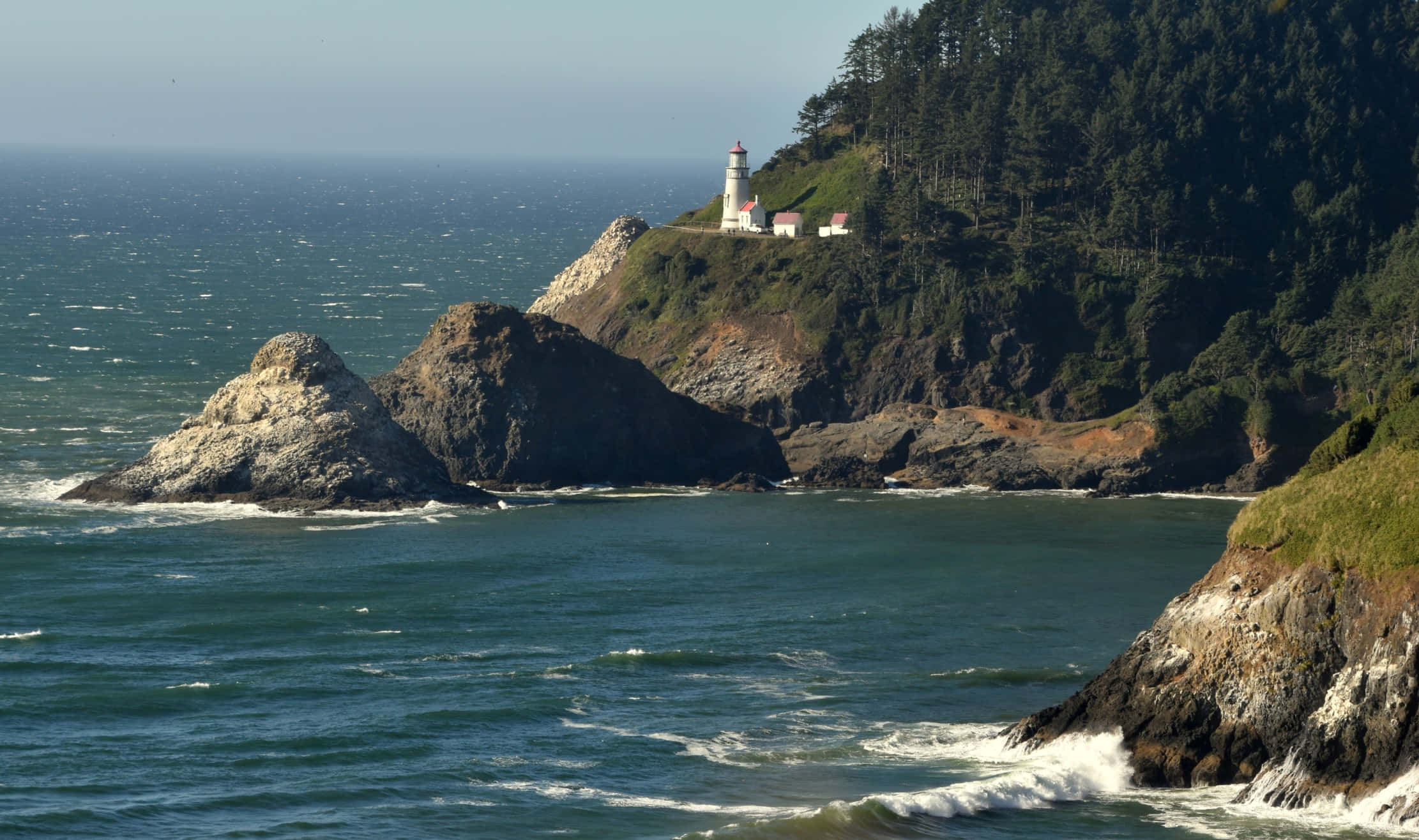 Oregon Coast 桌布 壁紙 — 一座白色燈塔矗立在崎嶇的懸崖上，俯瞰著波濤洶湧的海浪拍打岩石海岸。
