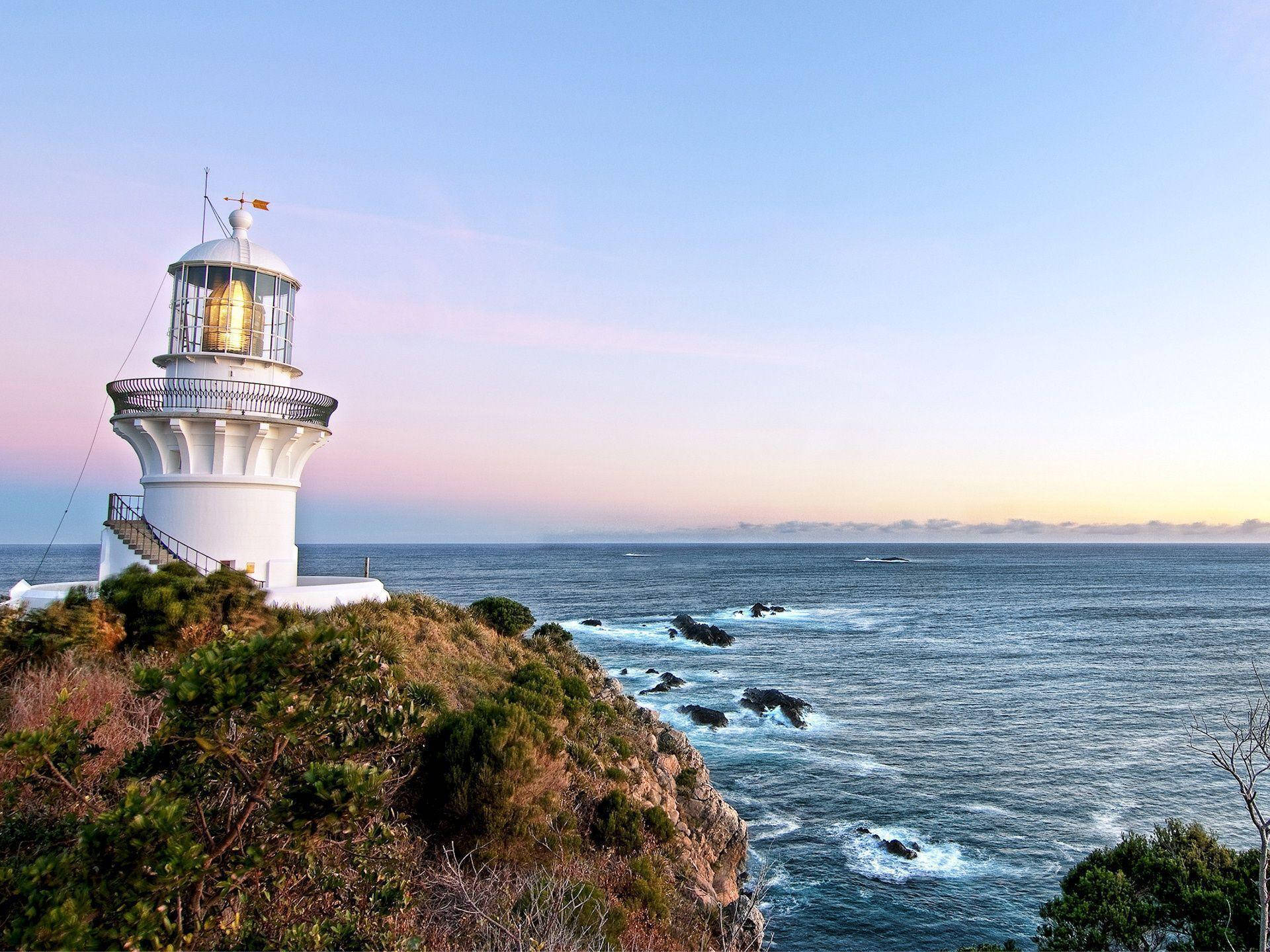 Lighthouse 桌布 壁紙 — 一座白色燈塔矗立在懸崖邊，俯瞰著在柔和粉紅與藍色暮色天空下翻騰的海浪。