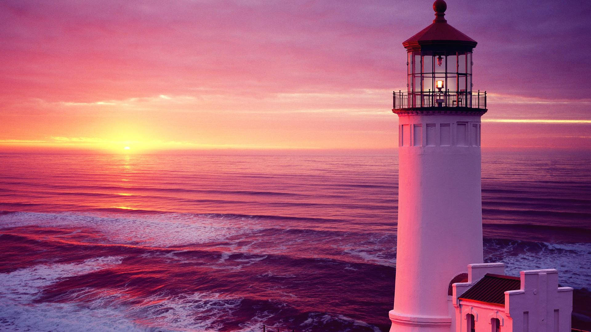 Lighthouse 桌布 壁紙 — 一座白色燈塔矗立在海洋上，背景是充滿活力的粉紅色和橙色日落，伴隨著輕柔的海浪。