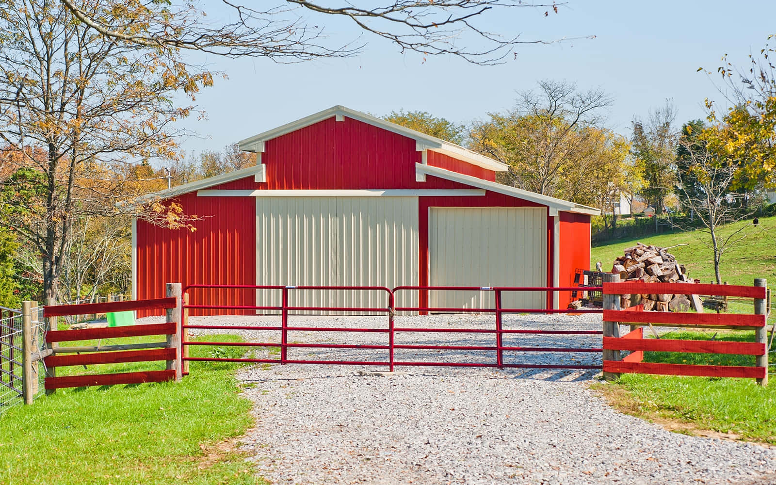 Barn 桌布 壁紙 — 一座白色門的鮮紅色穀倉矗立在碎石車道上，後面是一道相配的紅色大門，周圍環繞著秋樹。