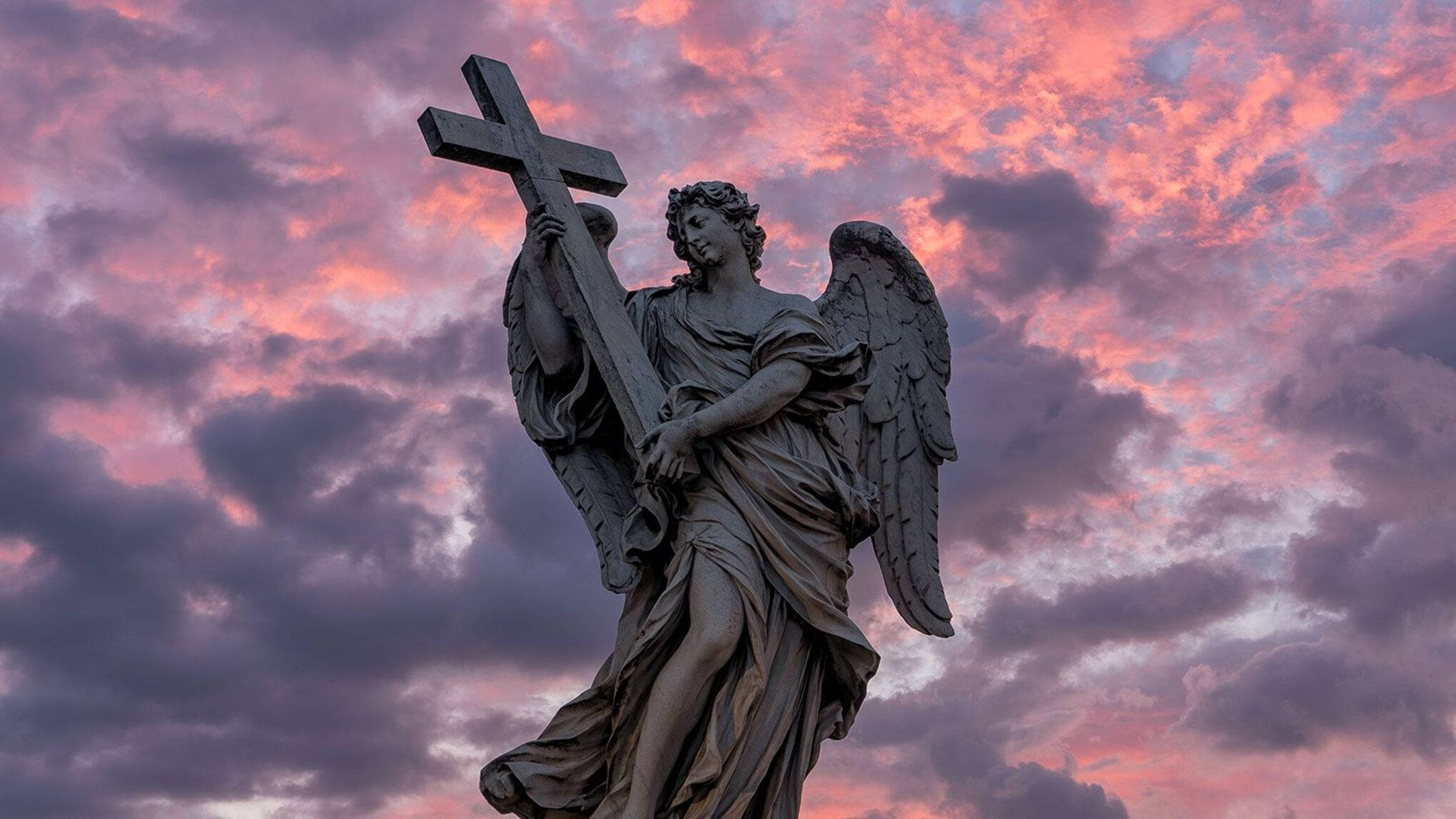 angels 桌布 壁紙 — 一座石天使雕像手持十字架，矗立在戲劇性的粉紅和紫色日落天空前。