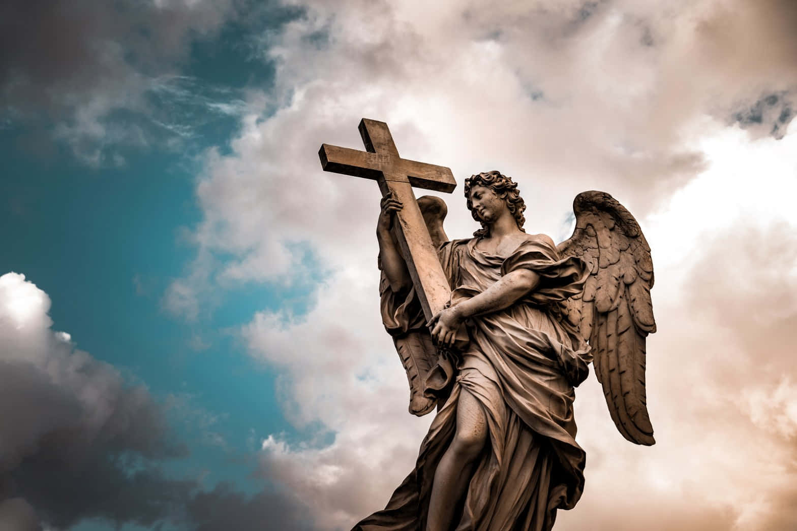 Religious Art 桌布 壁紙 — 一座石天使雕像手持十字架，矗立在戲劇性的天空下，天空有漩渦狀雲朵和藍綠色斑塊。