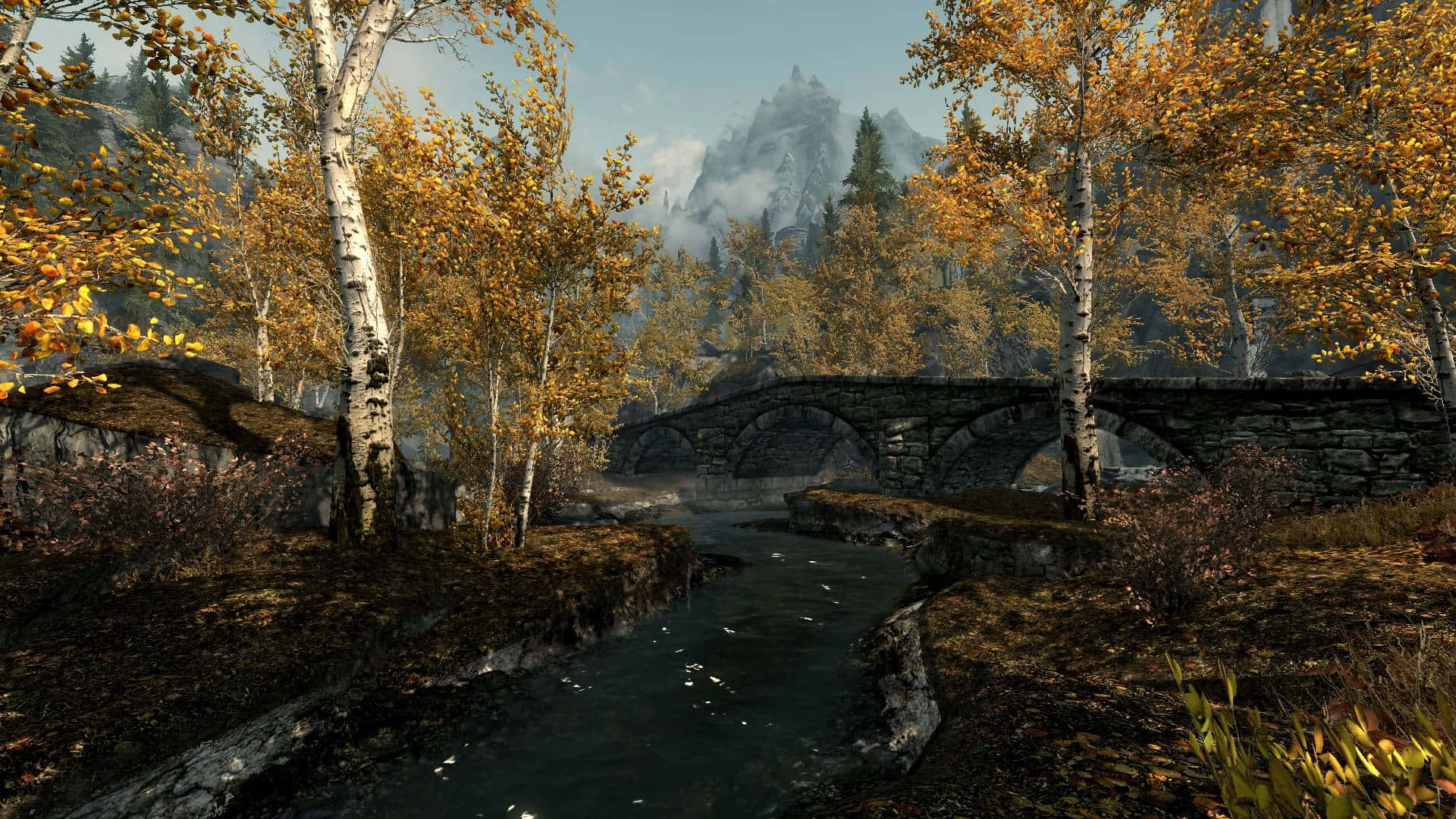 Skyrim Landscapes 桌布 壁紙 — 一座石橋拱跨在平靜的小溪上，周圍是金黃色的秋季白樺樹，背景是霧濛濛的山巒。