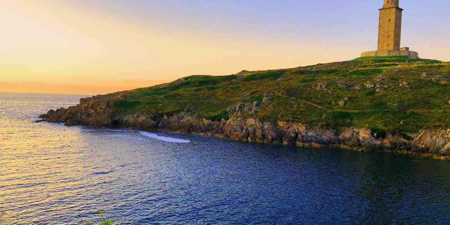 風景 桌布 壁紙 — 一座石燈塔矗立在長滿草的懸崖上，俯瞰著金色日落時分深藍色的海浪。