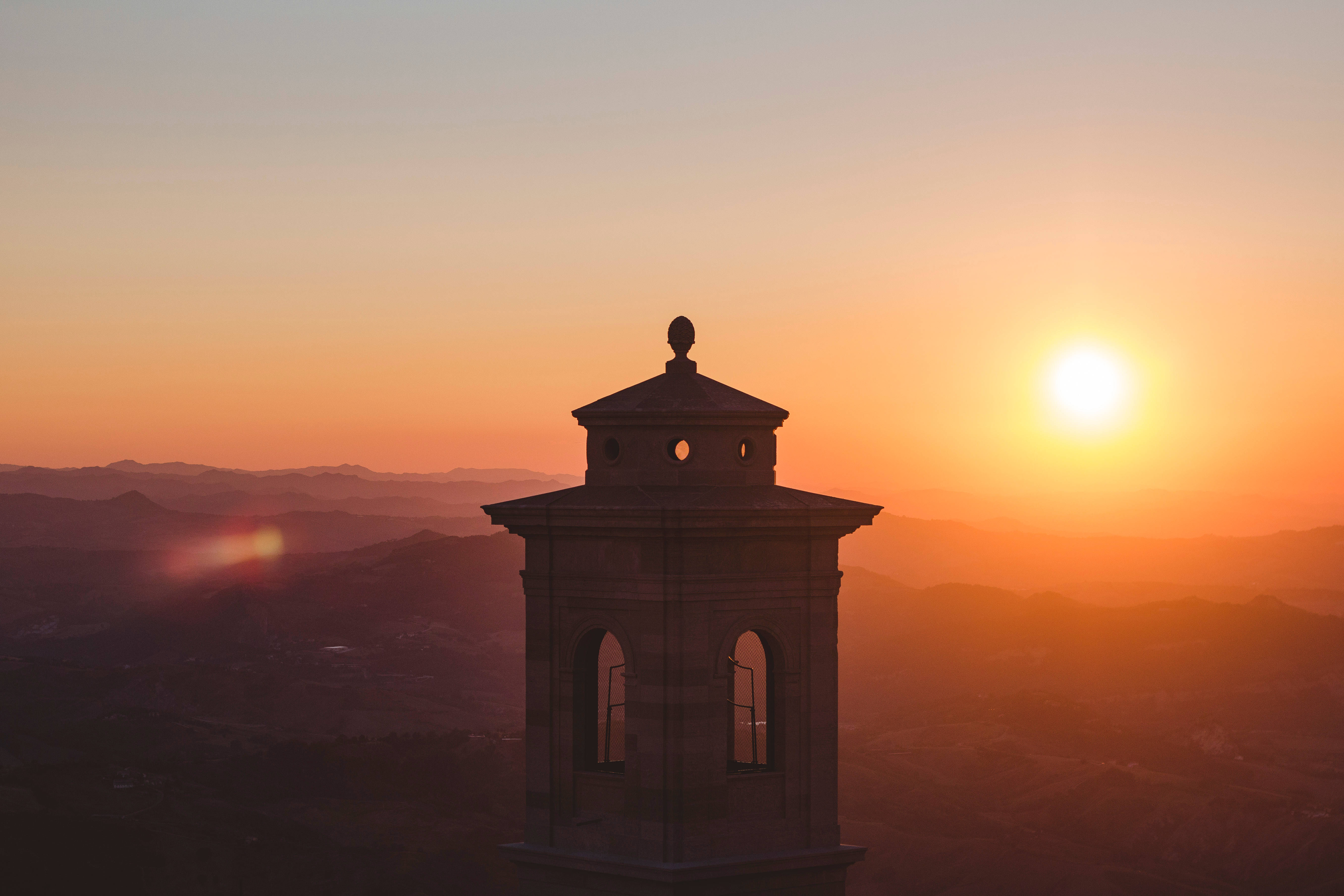San Marino 桌布 壁紙 — 一座石造鐘樓在起伏山丘上鮮豔橙色夕陽的襯托下形成剪影。