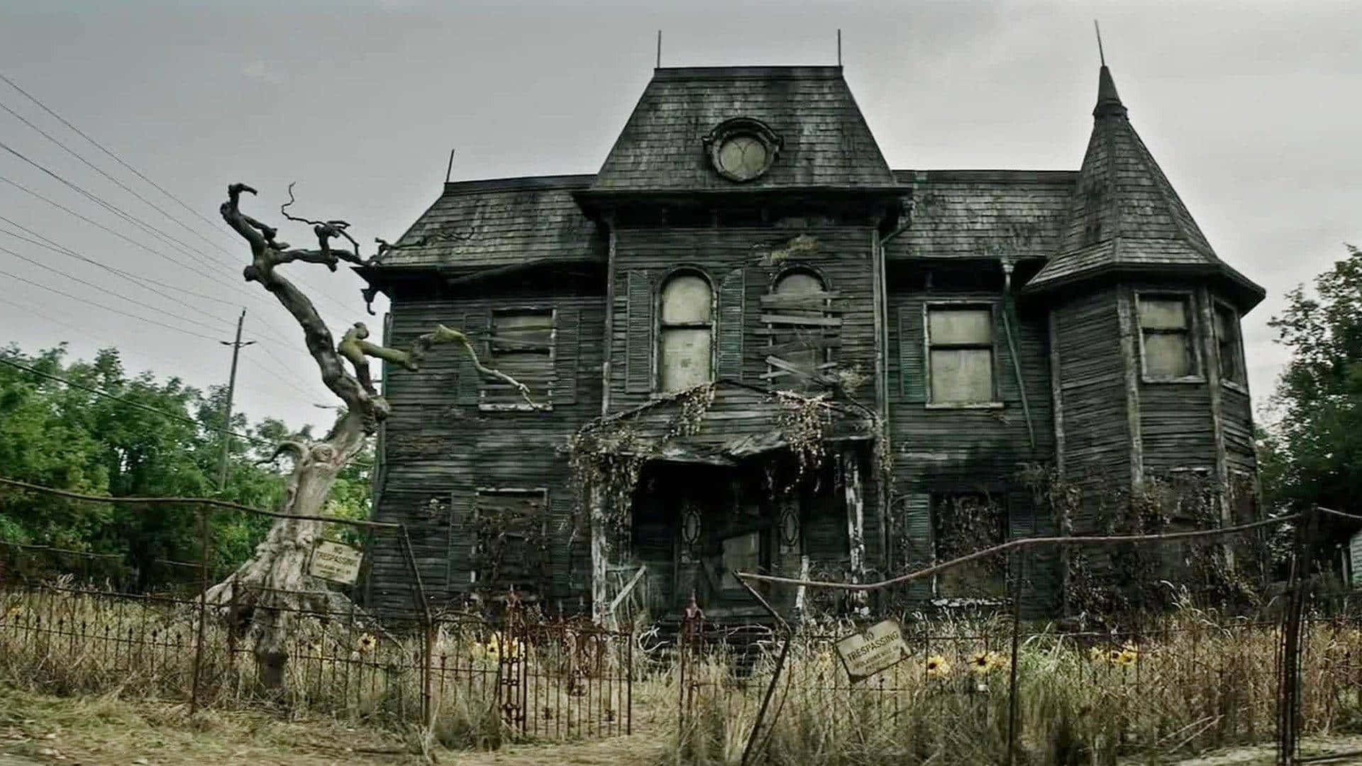 Haunted House 桌布 壁紙 — 一座破敗的維多利亞式大宅，窗戶破損，藤蔓叢生，矗立在陰沉天空下，周圍是野草和生鏽的圍欄。