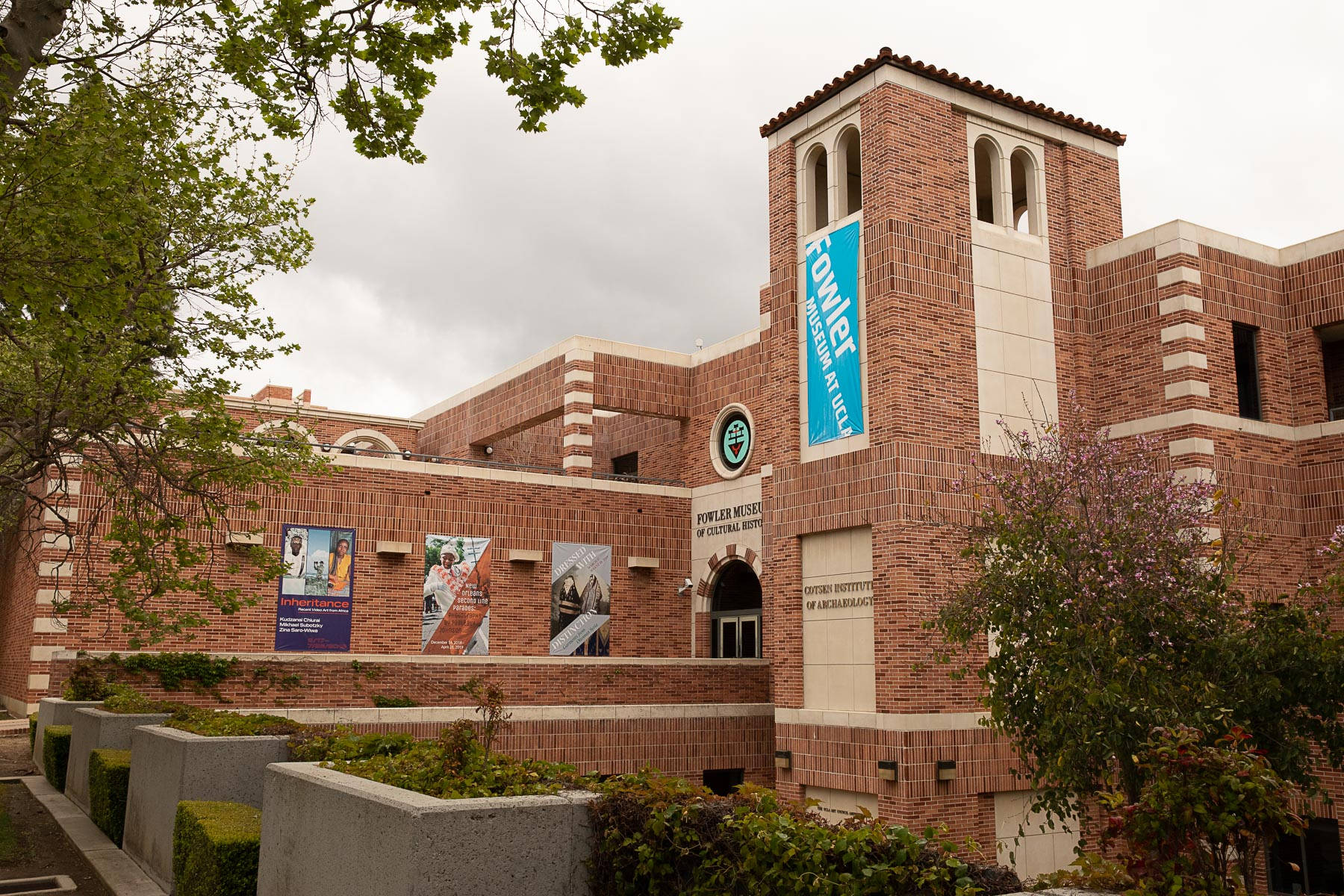 Museum 桌布 壁紙 — 一座磚砌大學博物館建築，帶有拱形窗戶和橫幅，位於多雲的天空下，周圍環繞著綠樹和灌木。