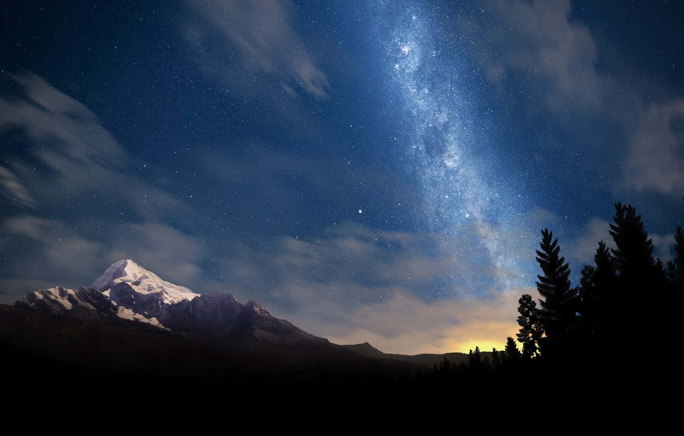 Beautiful Star 桌布 壁紙 — 一座積雪的山峰在璀璨星空下聳立，銀河在松樹剪影上方閃耀。