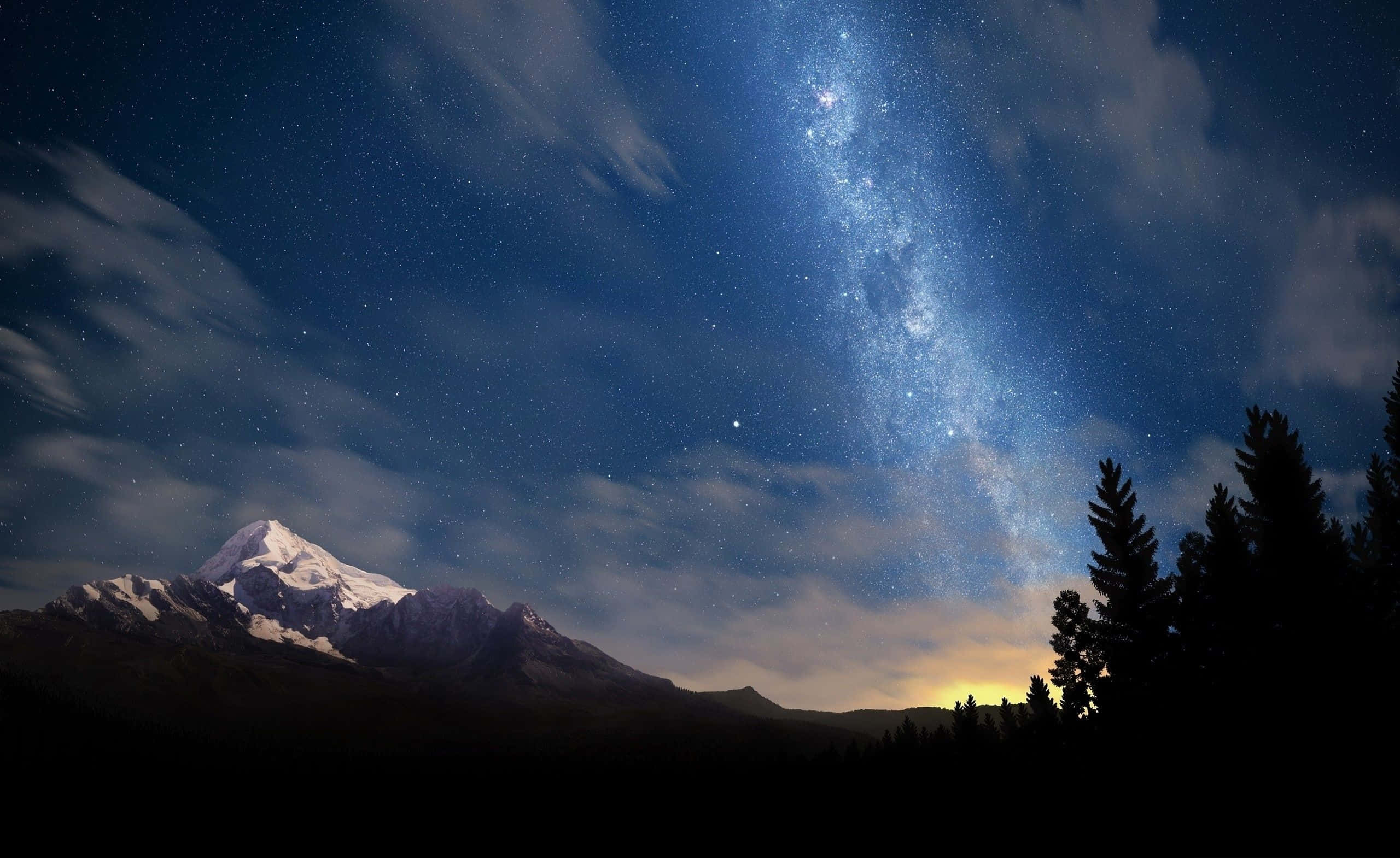 山景 桌布 壁紙 — 一座積雪的山峰在繁星閃爍的天空下升起，銀河在樹木剪影上方閃耀。