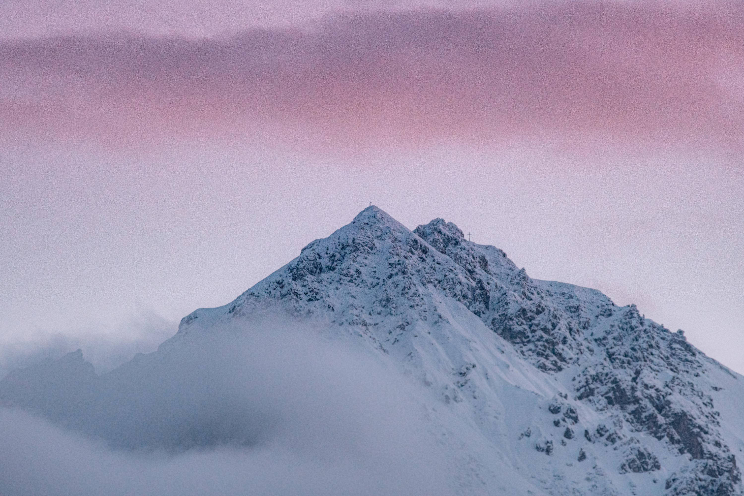 冬季桌面 桌布 壁紙 — 一座積雪的山峰在薄霧中升起，伴隨著黎明時分柔和的粉紅色和紫色天空。