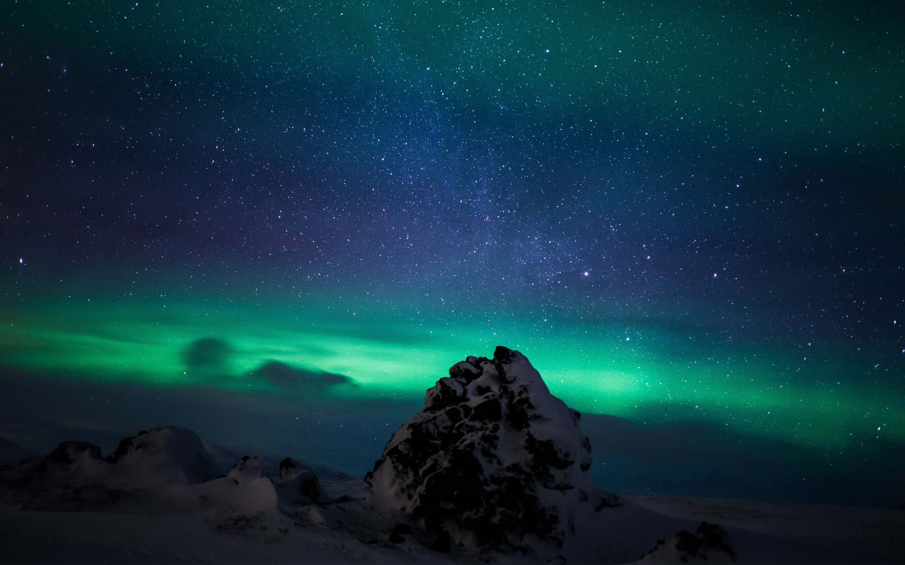 Aurora 桌布 壁紙 — 一座積雪的山峰矗立在充滿活力的綠色北極光下，北極光在繁星點點的夜空中舞動。