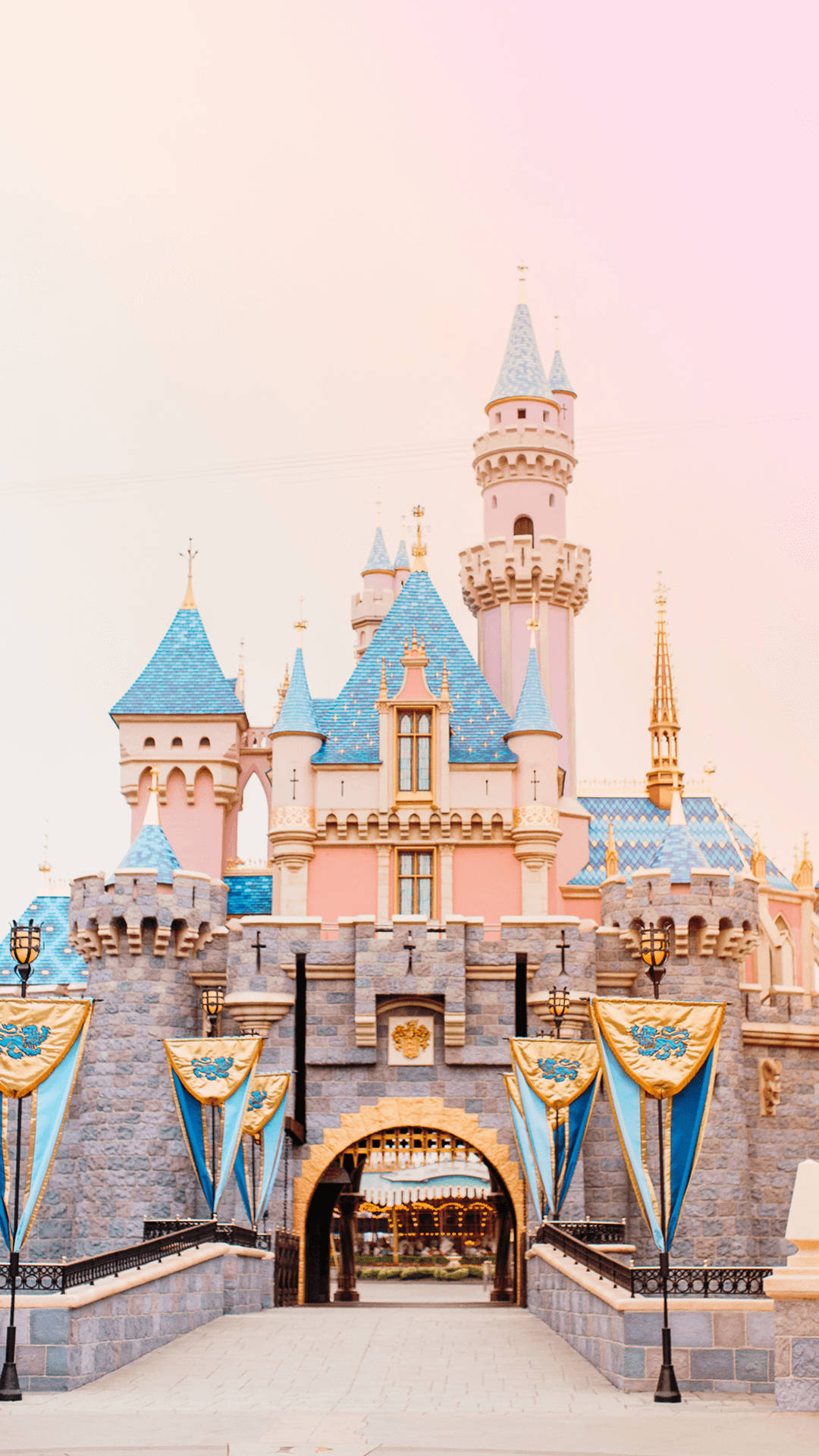 Castle 桌布 壁紙 — 一座童話城堡，粉紅色的牆壁和藍色的屋頂，矗立在柔和的粉紅色天空下，入口處懸掛著旗幟。