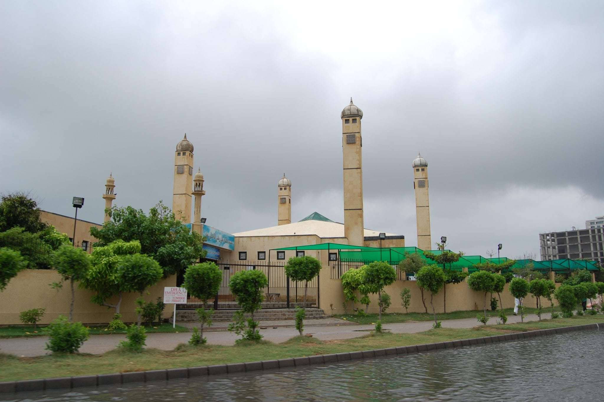 Karachi 桌布 壁紙 — 一座米色清真寺，有多個宣禮塔，矗立在平靜的運河旁，天空多雲。