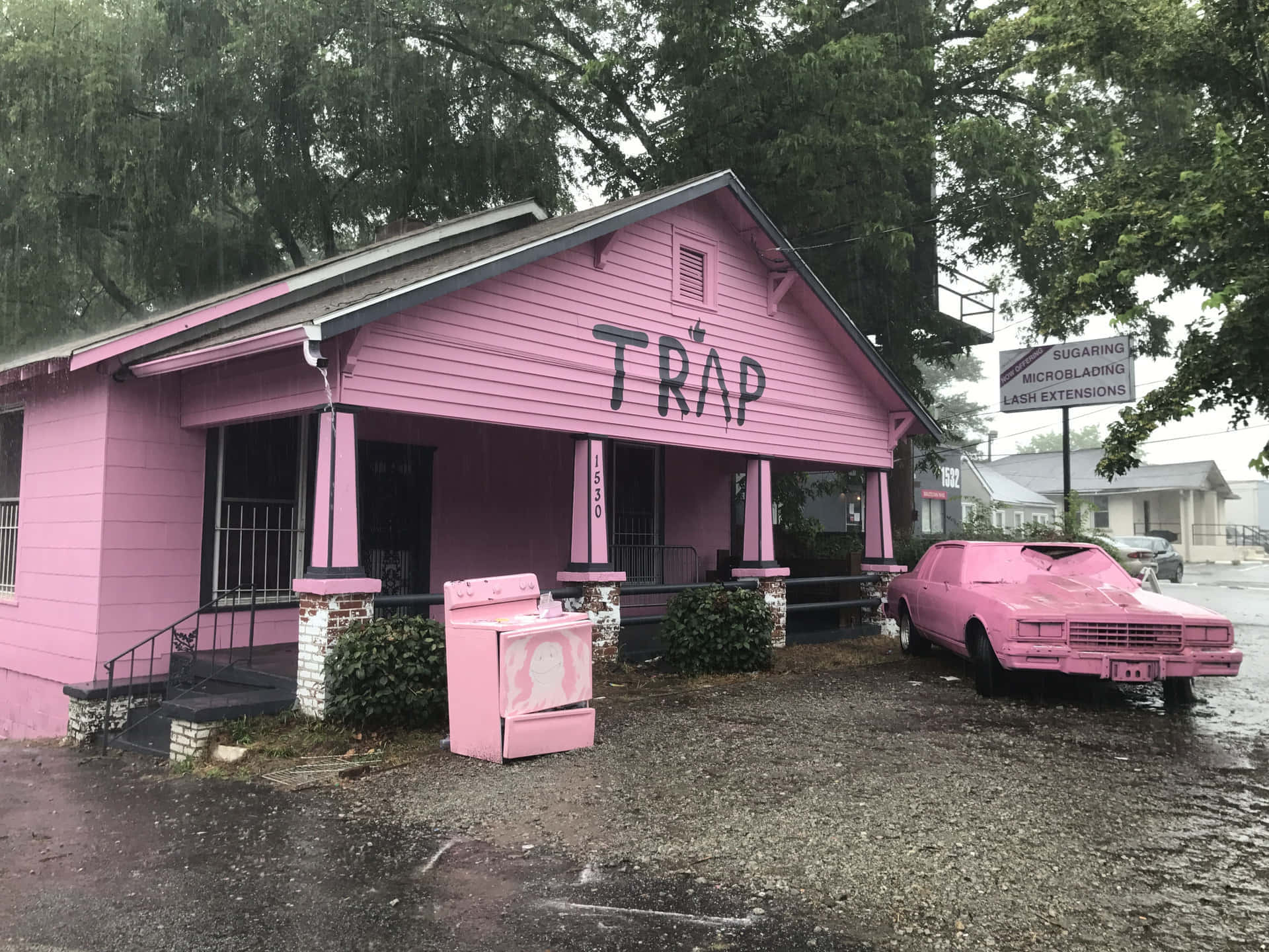 Trap House 桌布 壁紙 — 一座粉紅色建築物側面塗有「TRAP」字樣，在雨中矗立，外面停著一輛相配的粉紅色汽車和電器。