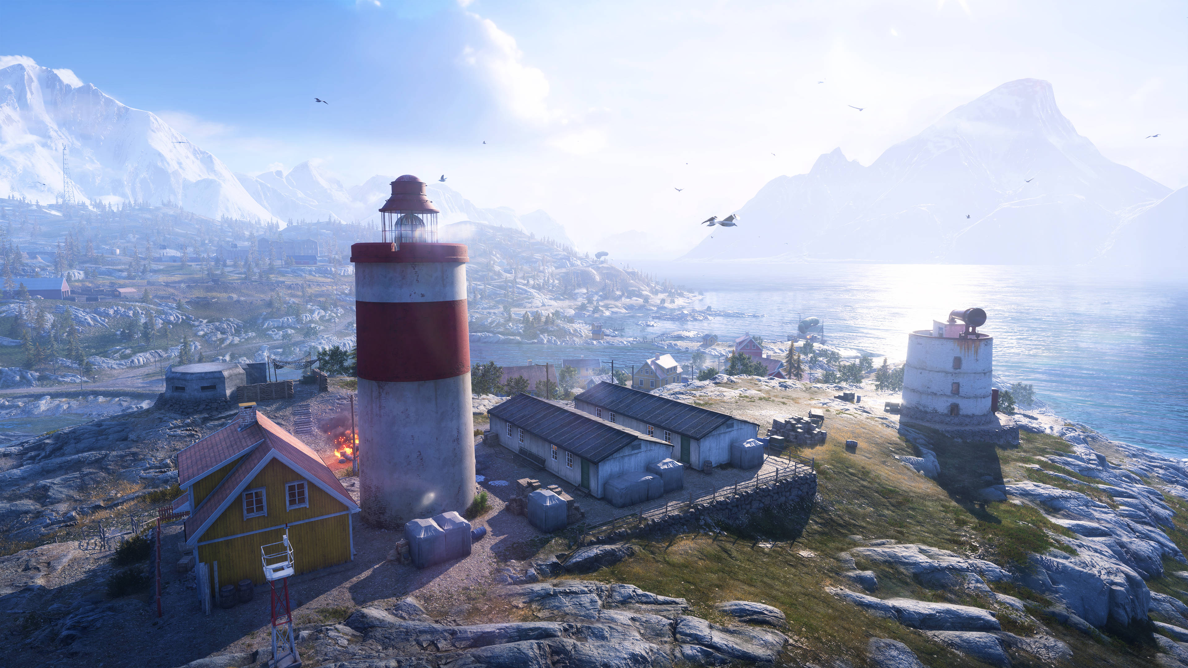 Battlefield 5 桌布 壁紙 — 一座紅白燈塔矗立在岩石峭壁上，俯瞰著一個沿海村莊，遠方有積雪覆蓋的山脈，在明亮的藍天下。