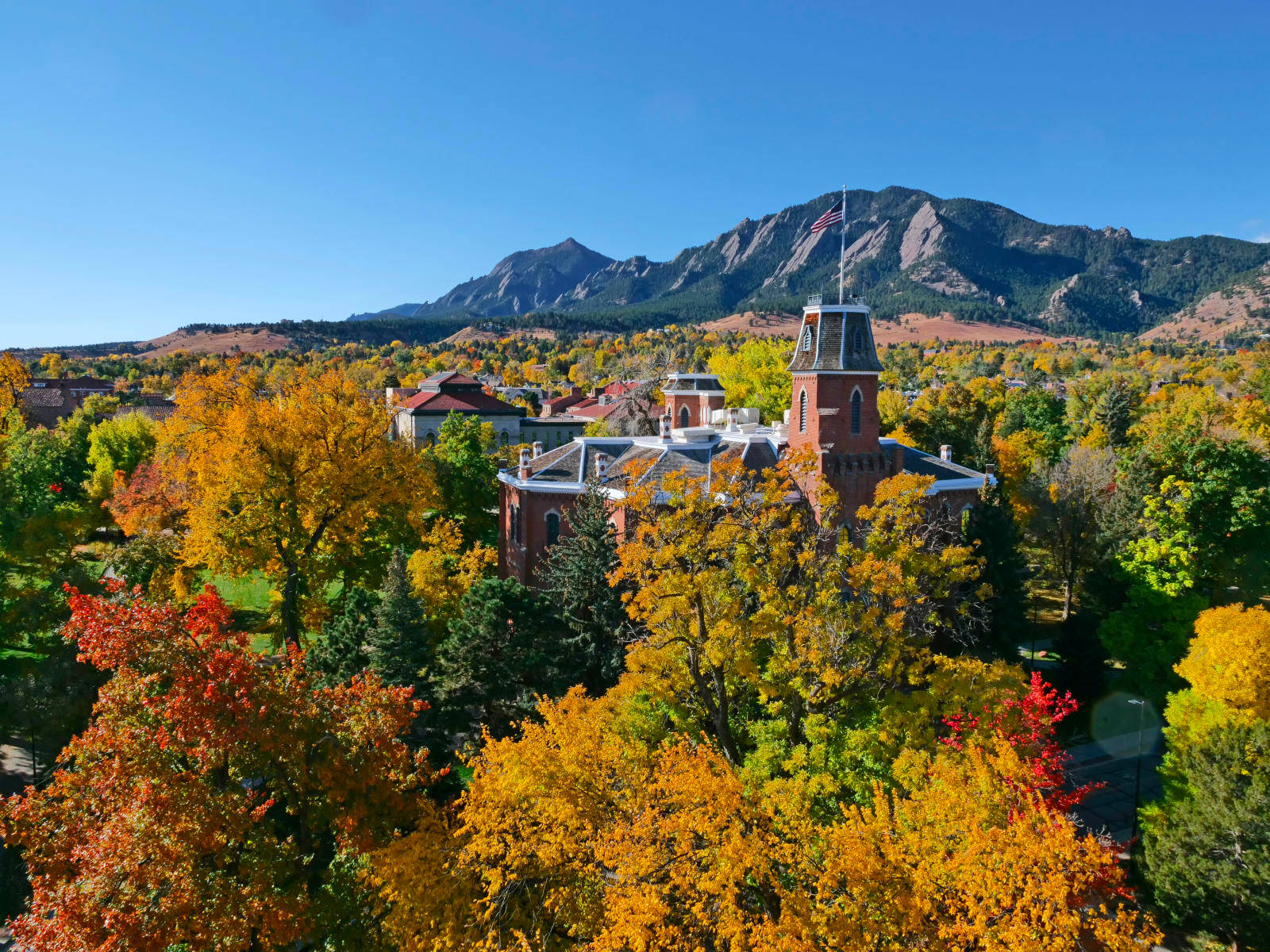 Colorado 桌布 壁紙 — 一座紅磚建築坐落在充滿活力的秋樹之中，山巒在清澈的藍天下聳立。