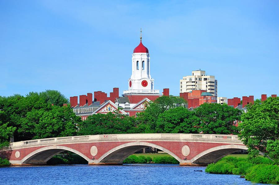 Massachusetts 桌布 壁紙 — 一座紅磚橋拱跨過平靜的河流，背景有歷史悠久的鐘樓和茂密的綠樹，在清澈的藍天下。